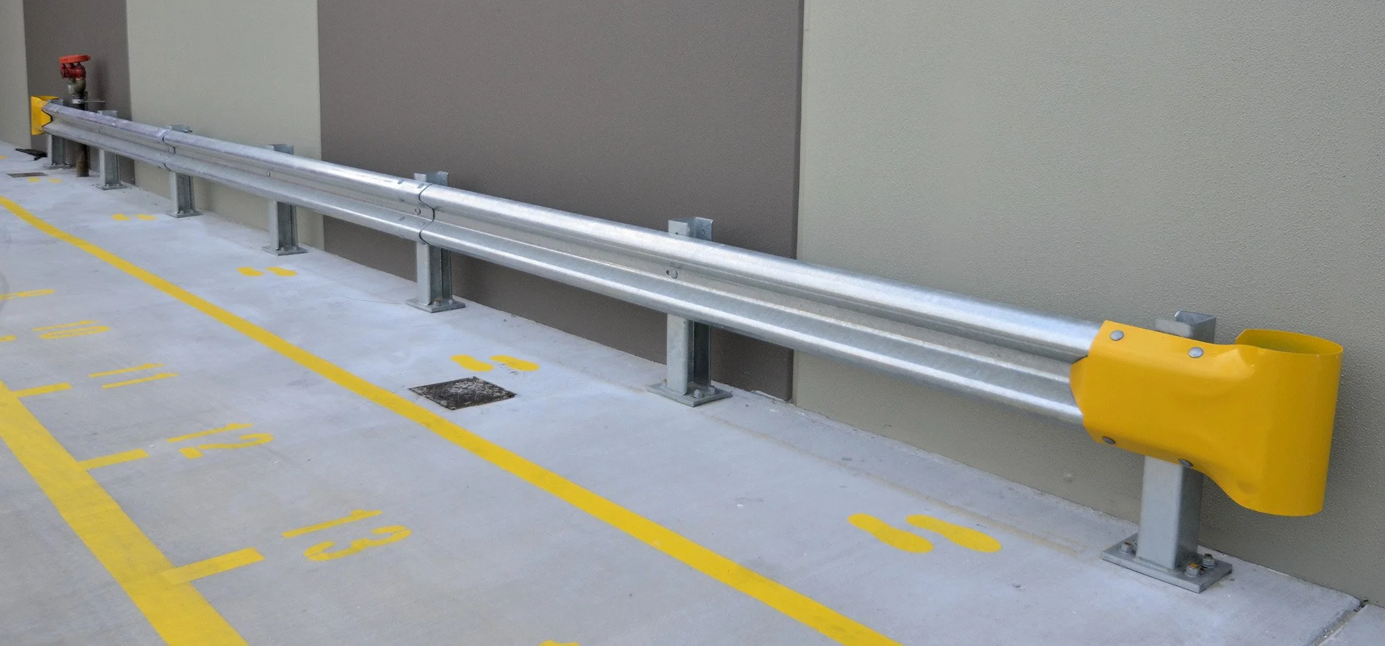 Empty designated parking spots marked with yellow lines and numbers next to a metal guardrail on a concrete parking deck.