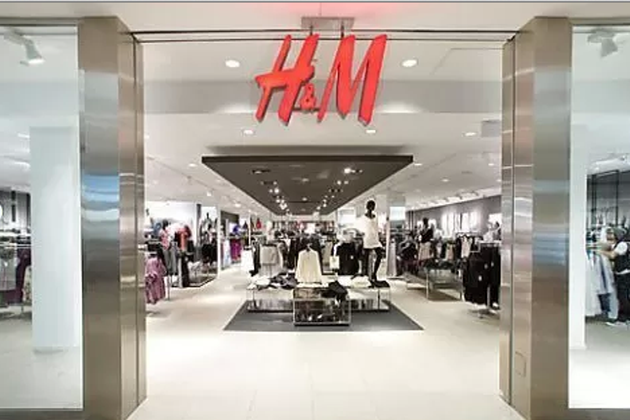 Entrance of an H&M clothing store inside a shopping mall, displaying various racks of clothes and mannequins.