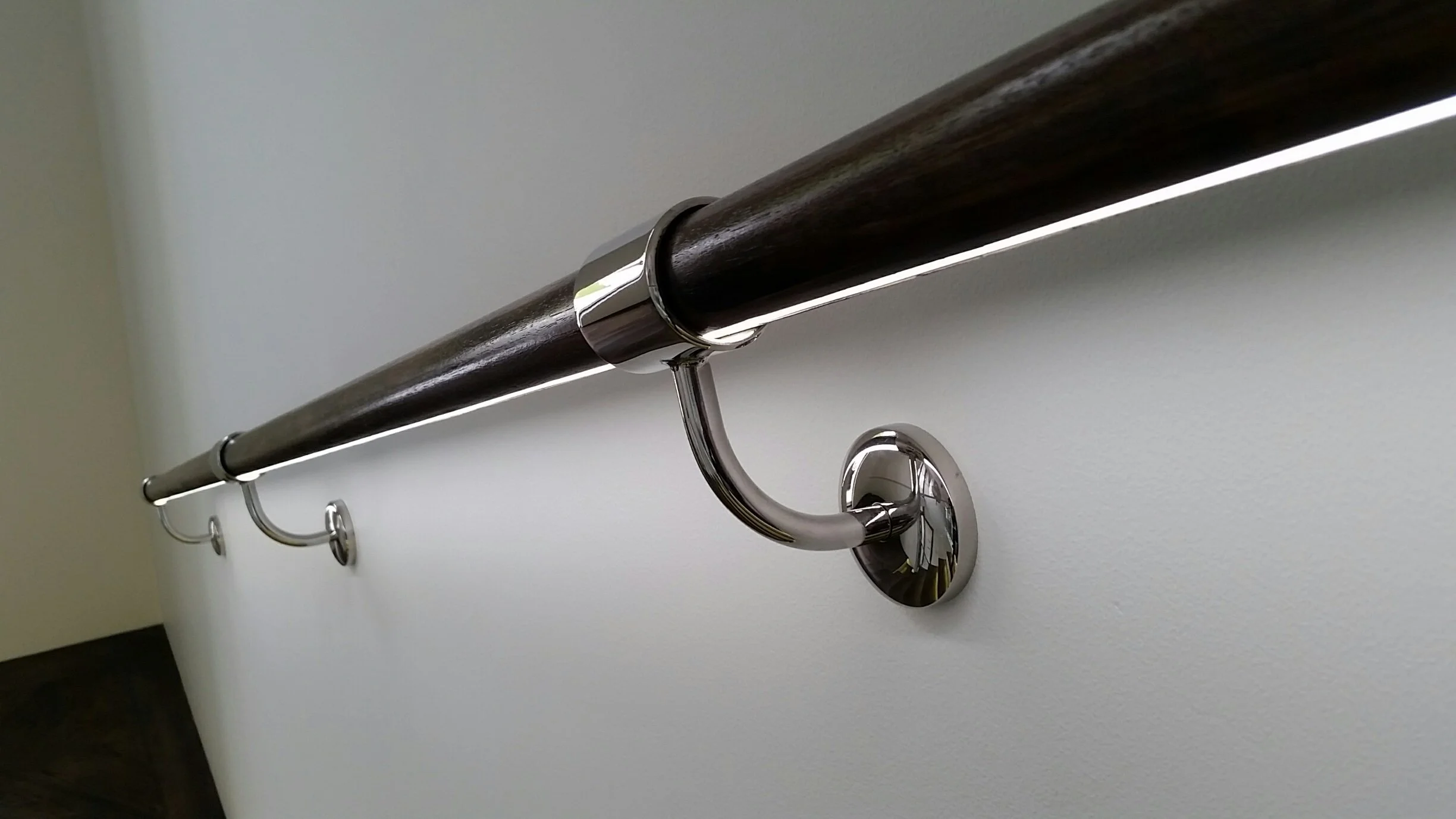 Close-up of a wooden and metal handrail with chrome brackets mounted on a white wall.