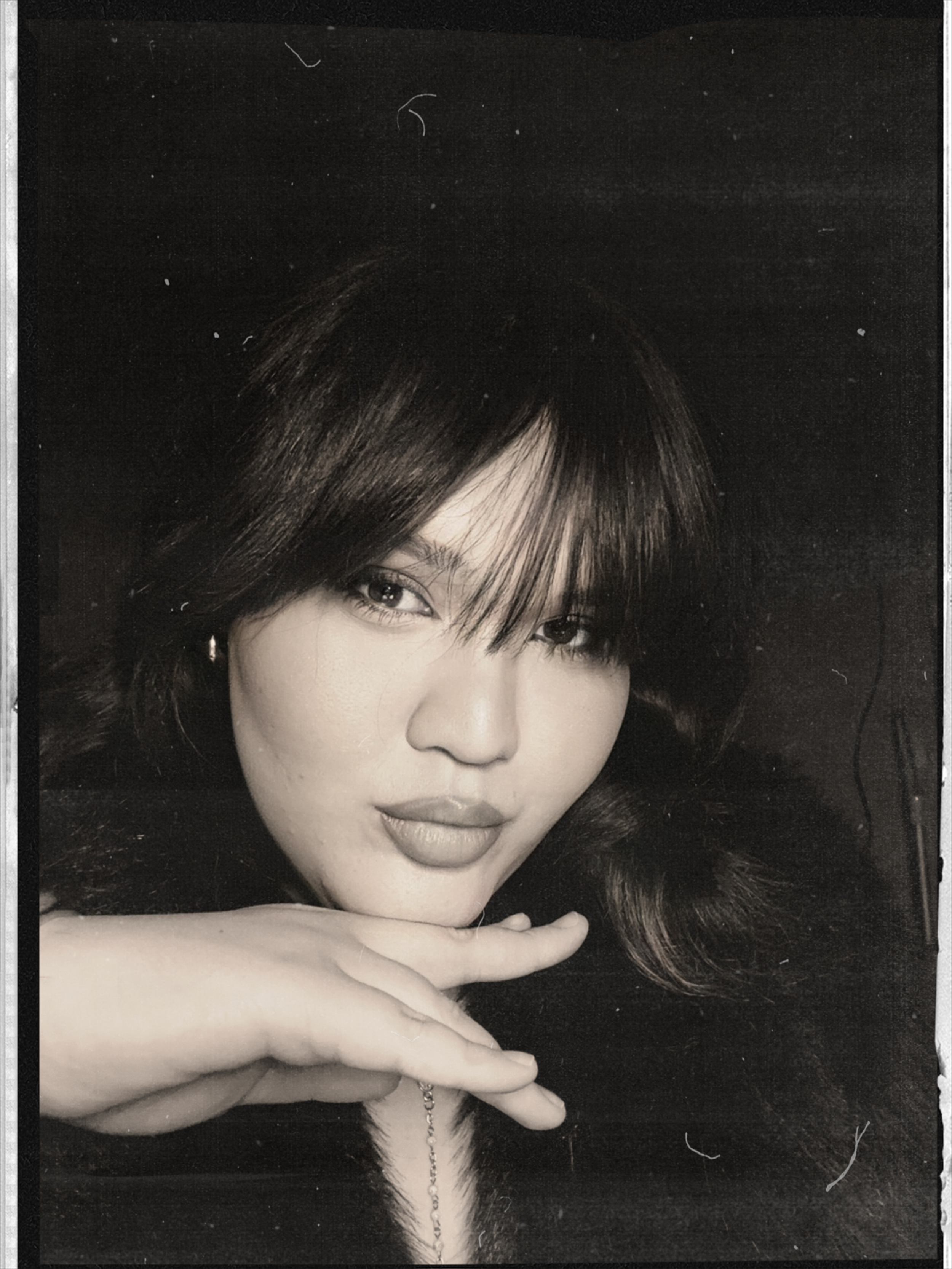 Black and white portrait of a person with dark hair, posing with a hand near their face.