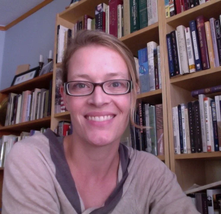 Woman wiht glasses and a tan blouse in front of a bookcase