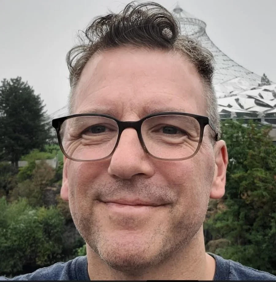 Man with black-framed glasses and dark gray shirt