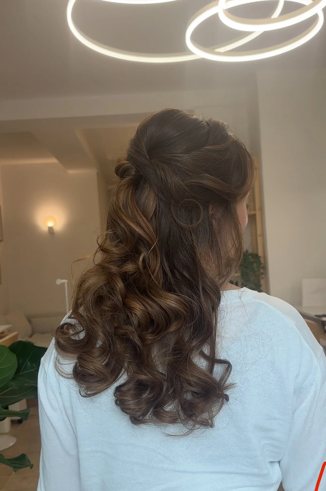 Frau mit braunen, lockigen Haaren, die halboffen gestylt sind, in einem hellen Raum mit moderner Beleuchtung