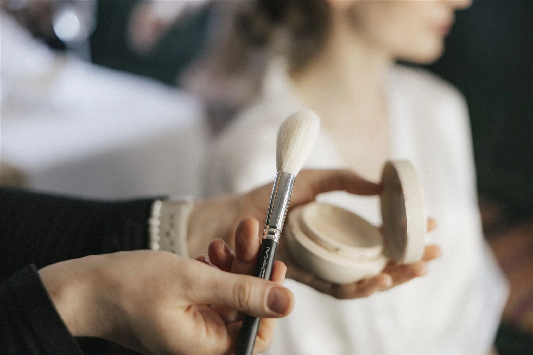 Jemand trägt Puder auf einen Frauen-Make-up-Pinsel auf, während eine Frau gerade Make-up auf ihrem Gesicht anwendet.