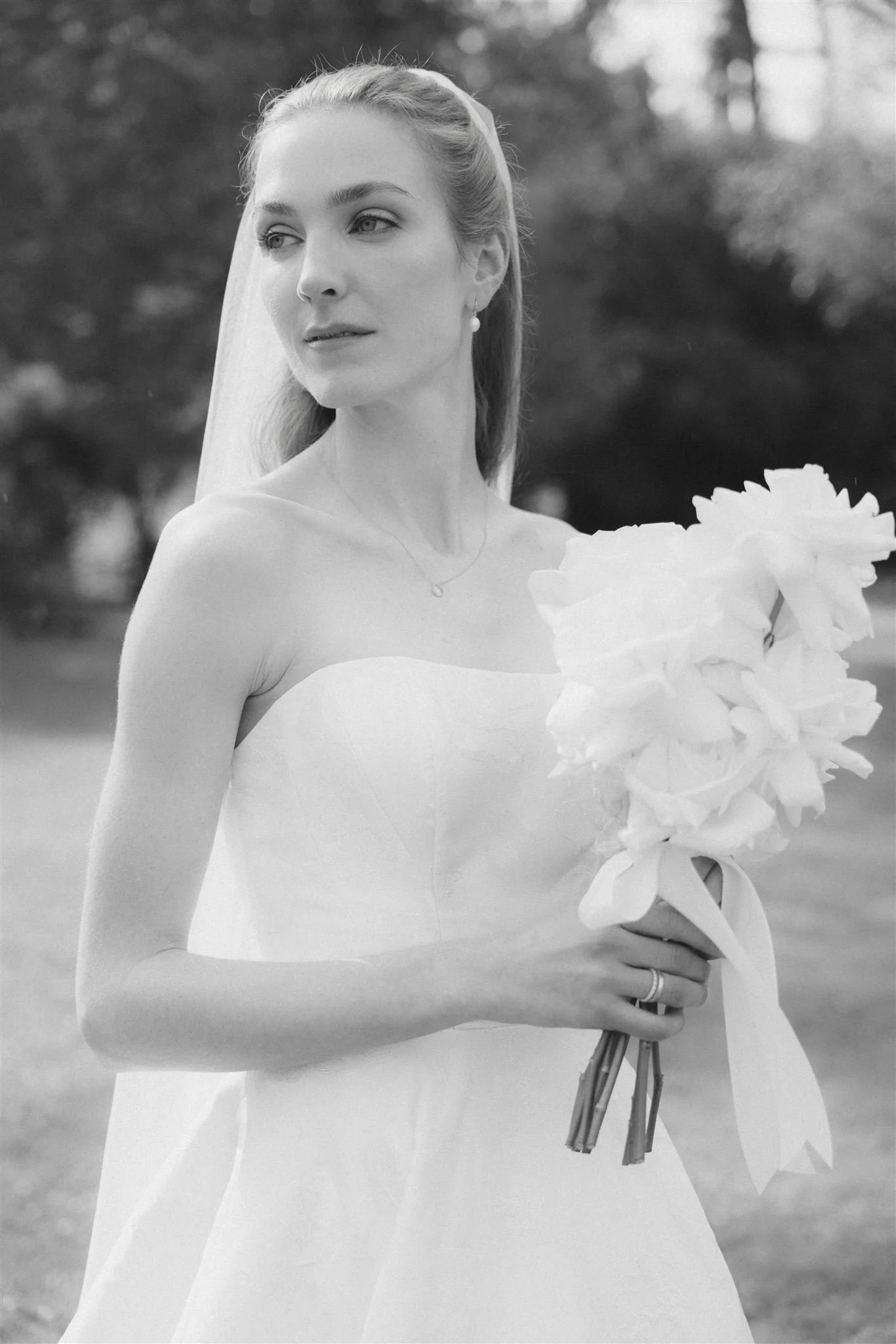 Eine junge Frau in einem Hochzeitskleid hält einen Blumenstrauß und steht im Freien.