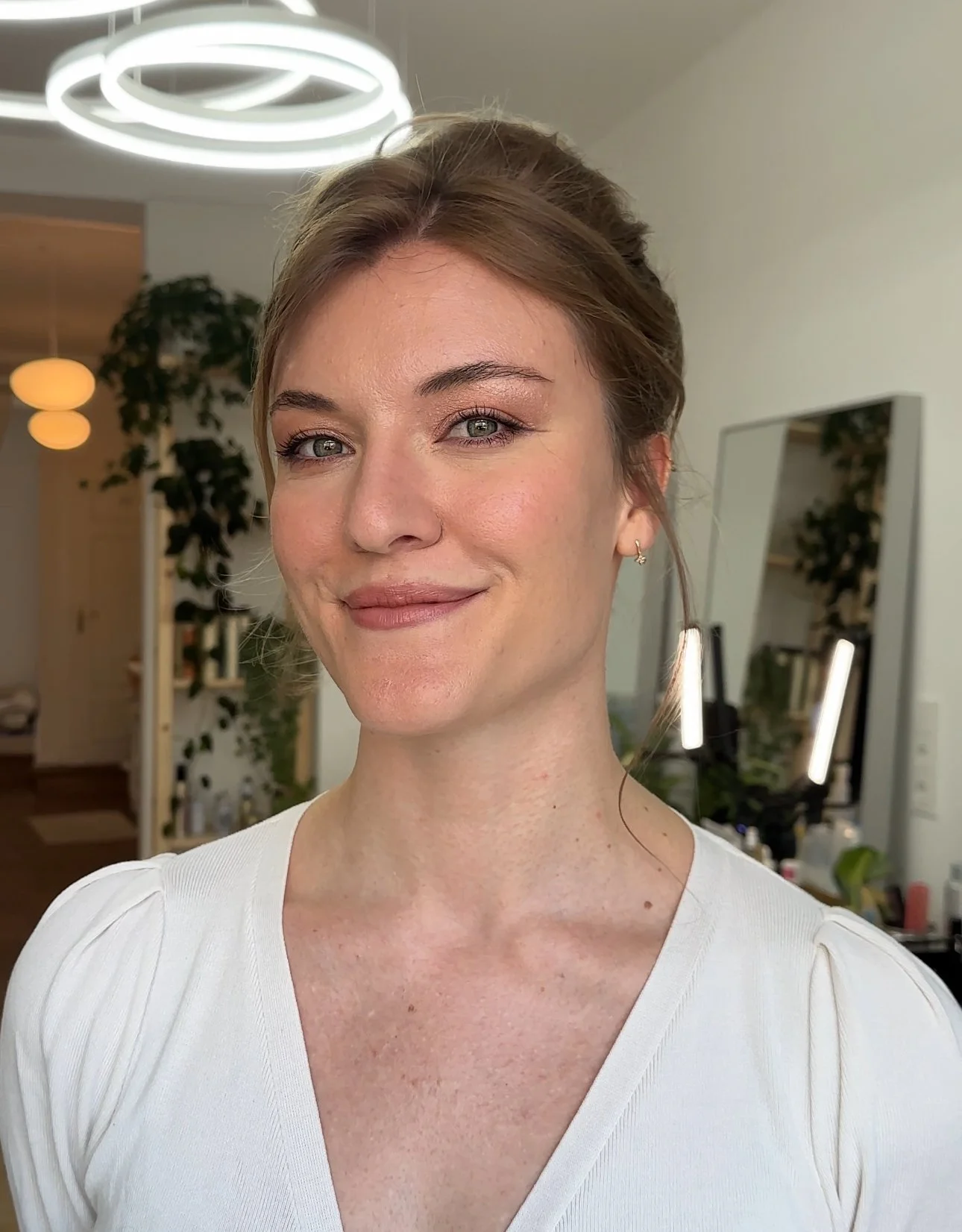 Nahaufnahme einer lächelnden jungen Frau mit braunen Haaren und blauen Augen in einem eleganten Raum.