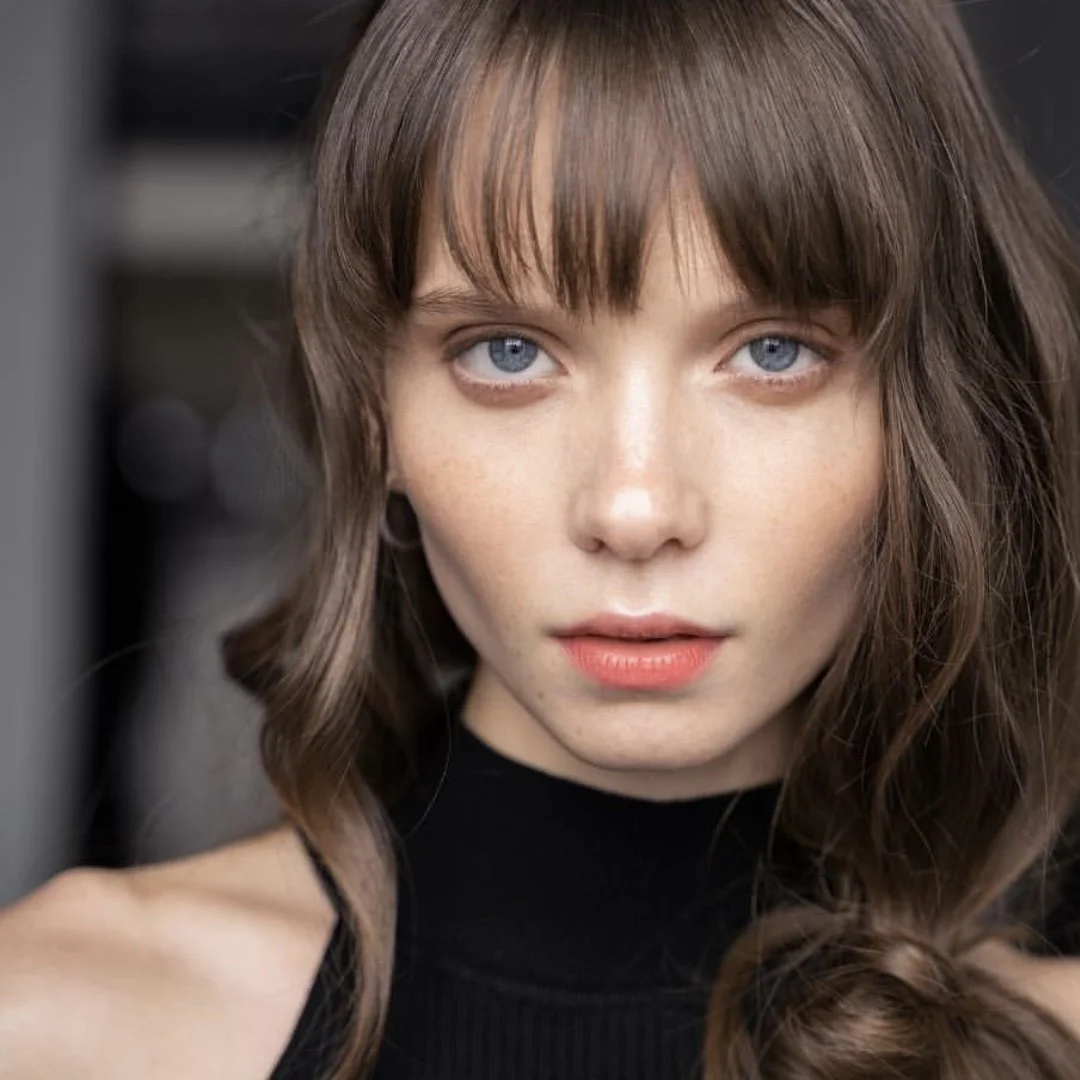 Nahaufnahme eines jungen Mädchens mit blauen Augen und braunen, gewellten Haaren