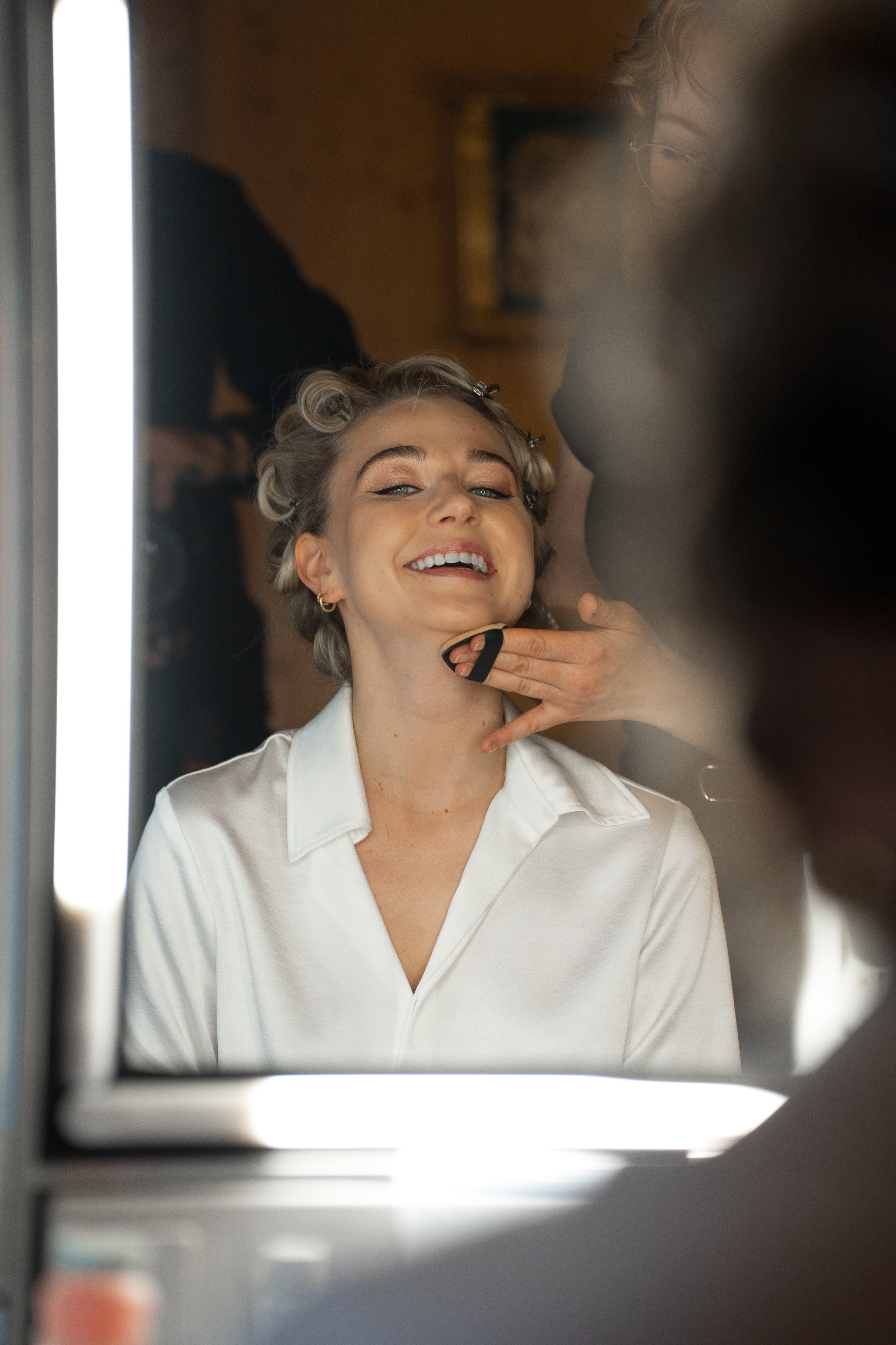 Frau bei einem Friseurbesuch, lächelnd in den Spiegel blickend, während Stylisten sie frisieren.