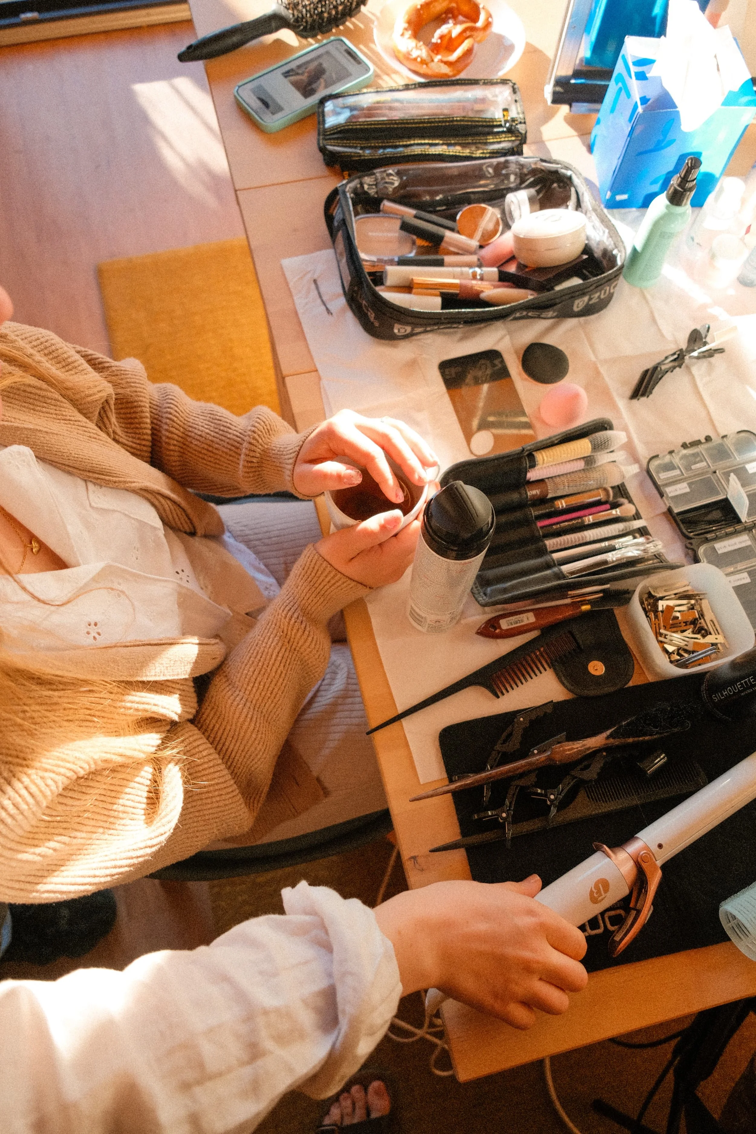 Ein zusammengelegener Tisch mit Make-up-Produkten, Pinsel, Spray, Handy und anderen Kosmetikartikeln, während zwei Personen ihre Produkte verwenden.