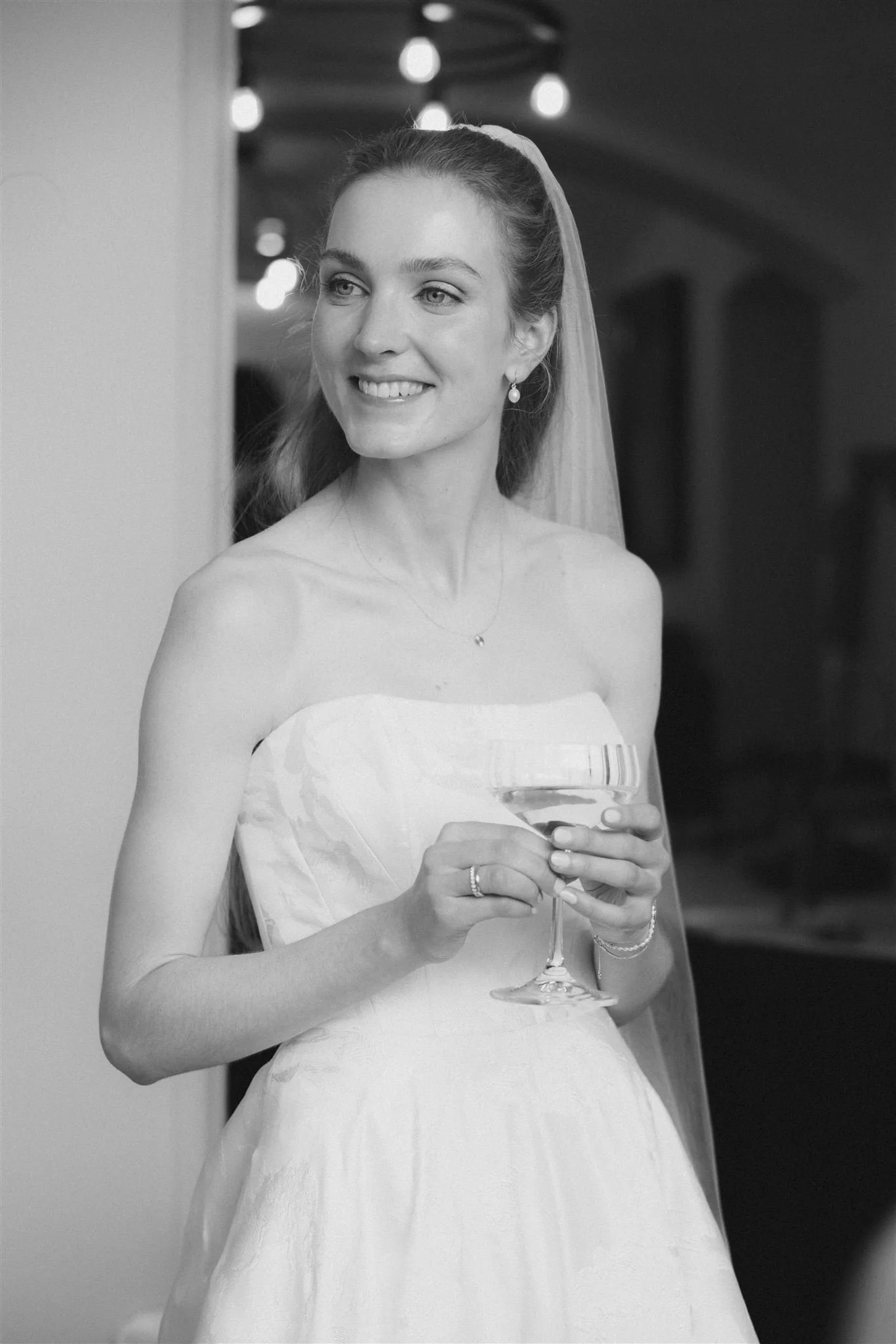 Braut in Hochzeitskleid hält ein Champagnerglas und lächelt.