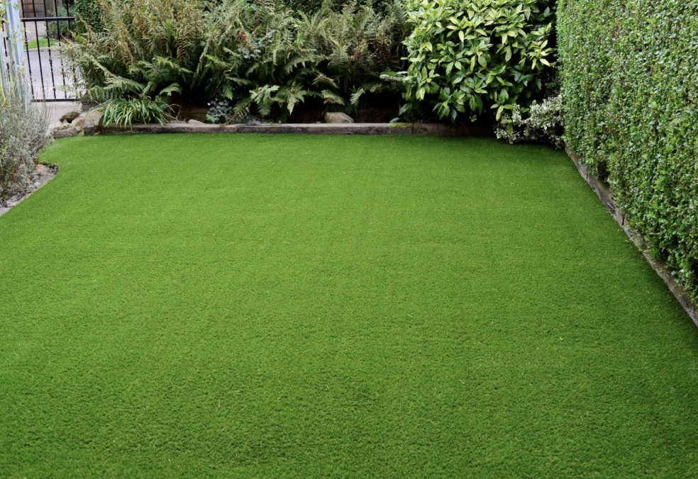Artificial grass lawn bordered by hedges and plants in a backyard garden.
