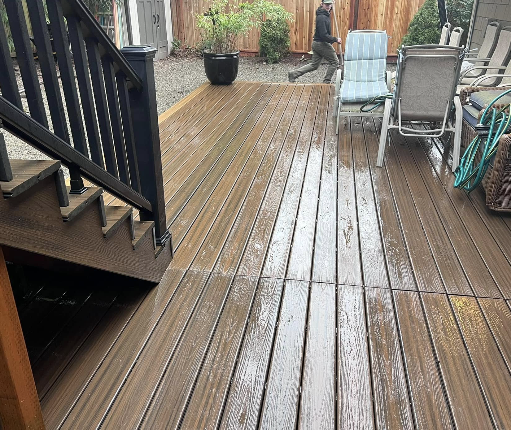 Wet wooden deck with stairs, patio furniture, garden hose, and potted plant