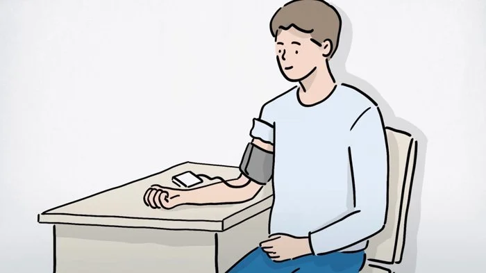 En mand sidder i en stol ved et bord med en blodtryksmåler på armen.