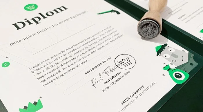 En diplom udskrevet til en borger i Skive kommune, med en grøn skildring af forskellige illustrationer som et tøjstykke, et ansigt og en sæk, og en stempel med tekst.