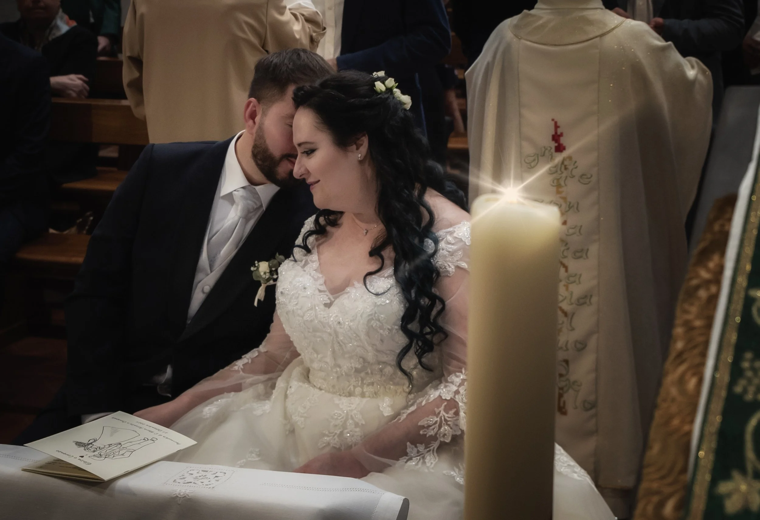 Sposi durante una cerimonia matrimoniale in chiesa con candelina accesa in primo piano.