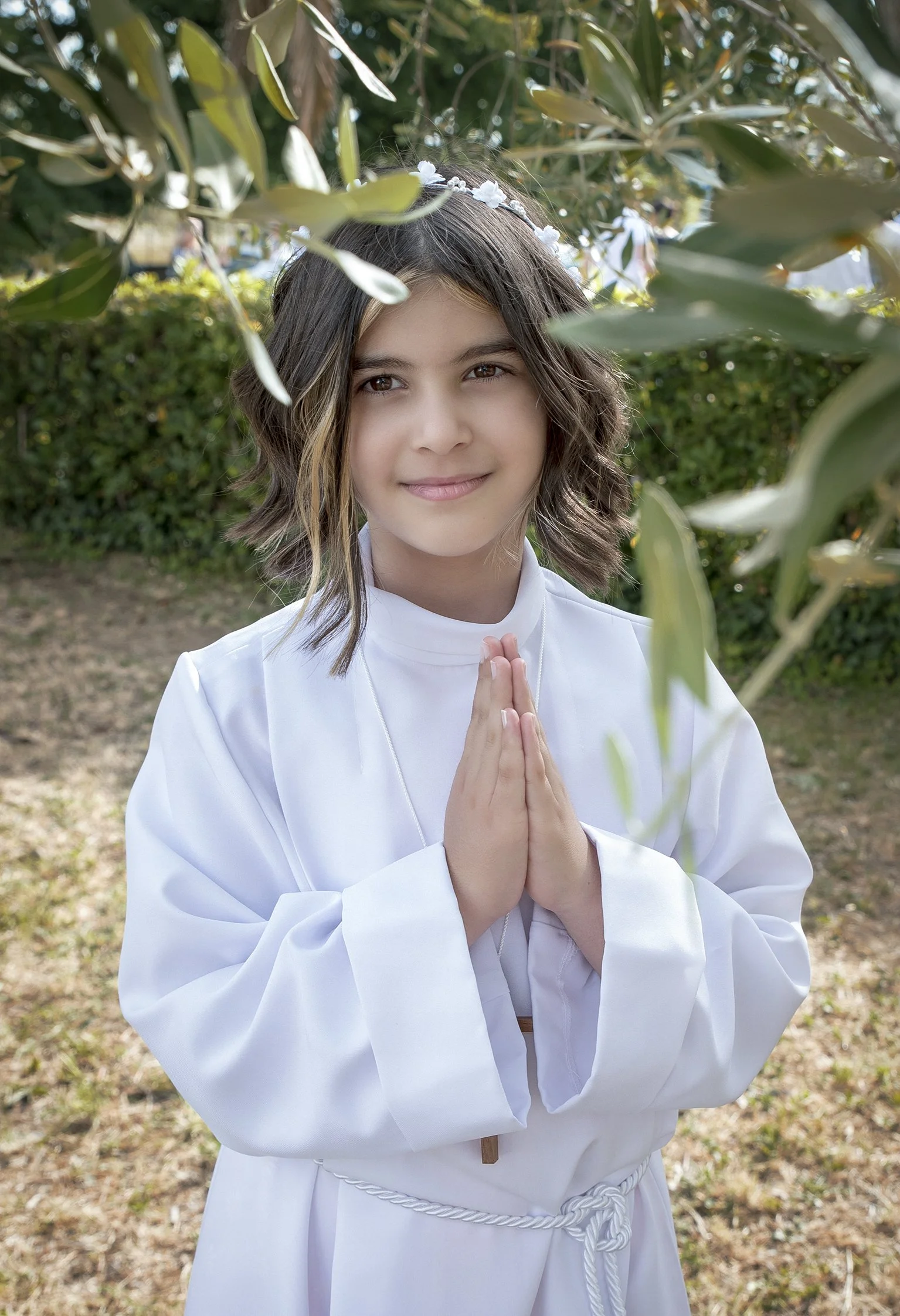 Bambina in abito bianco per la Prima Comunione con le mani giunte.