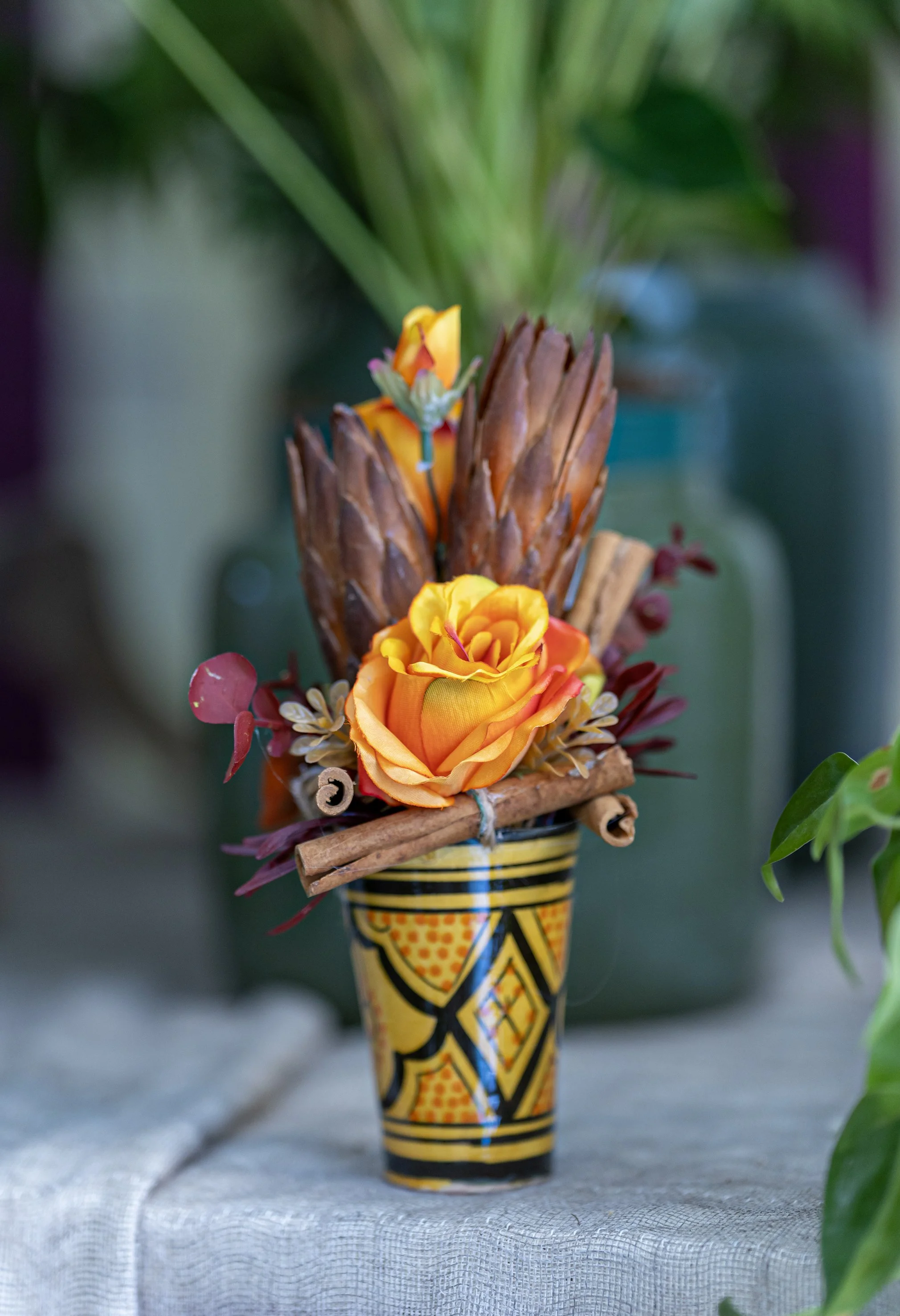Composizione floreale con rosa arancione, fiori secchi e bastoncini di cannella in vaso decorativo.