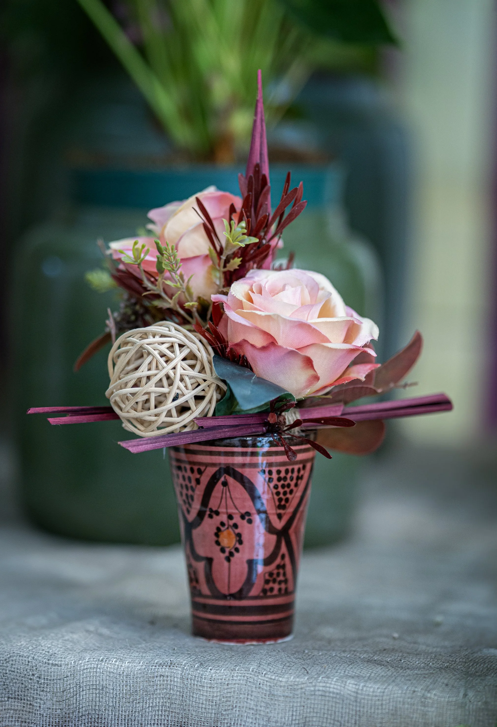 Bouquet di fiori artificiali in un vaso decorativo, con rose rosa e decorazioni naturali, su uno sfondo sfocato.