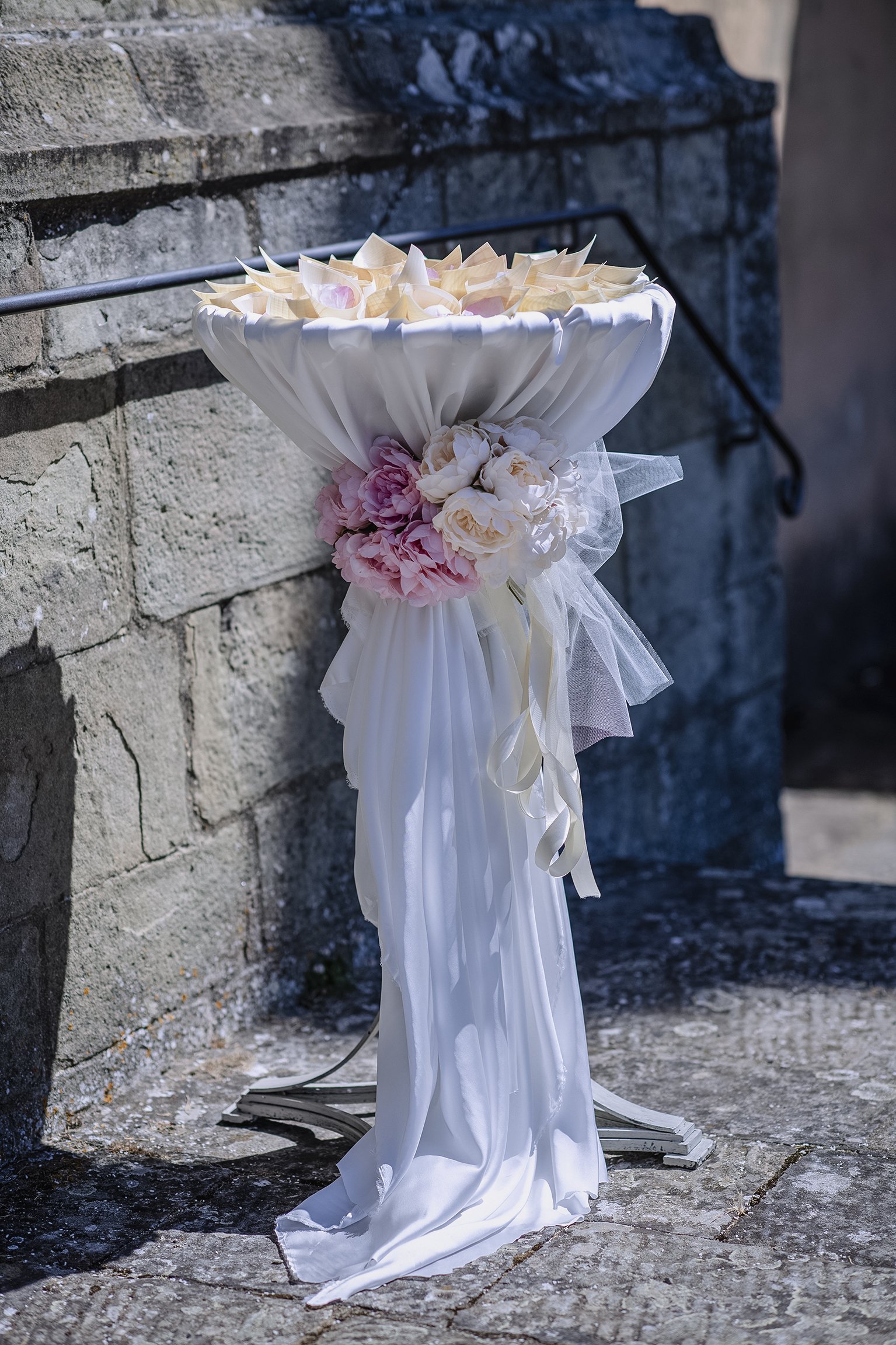 Supporto decorato con fiori e tessuto bianco, su fondo di pietra.