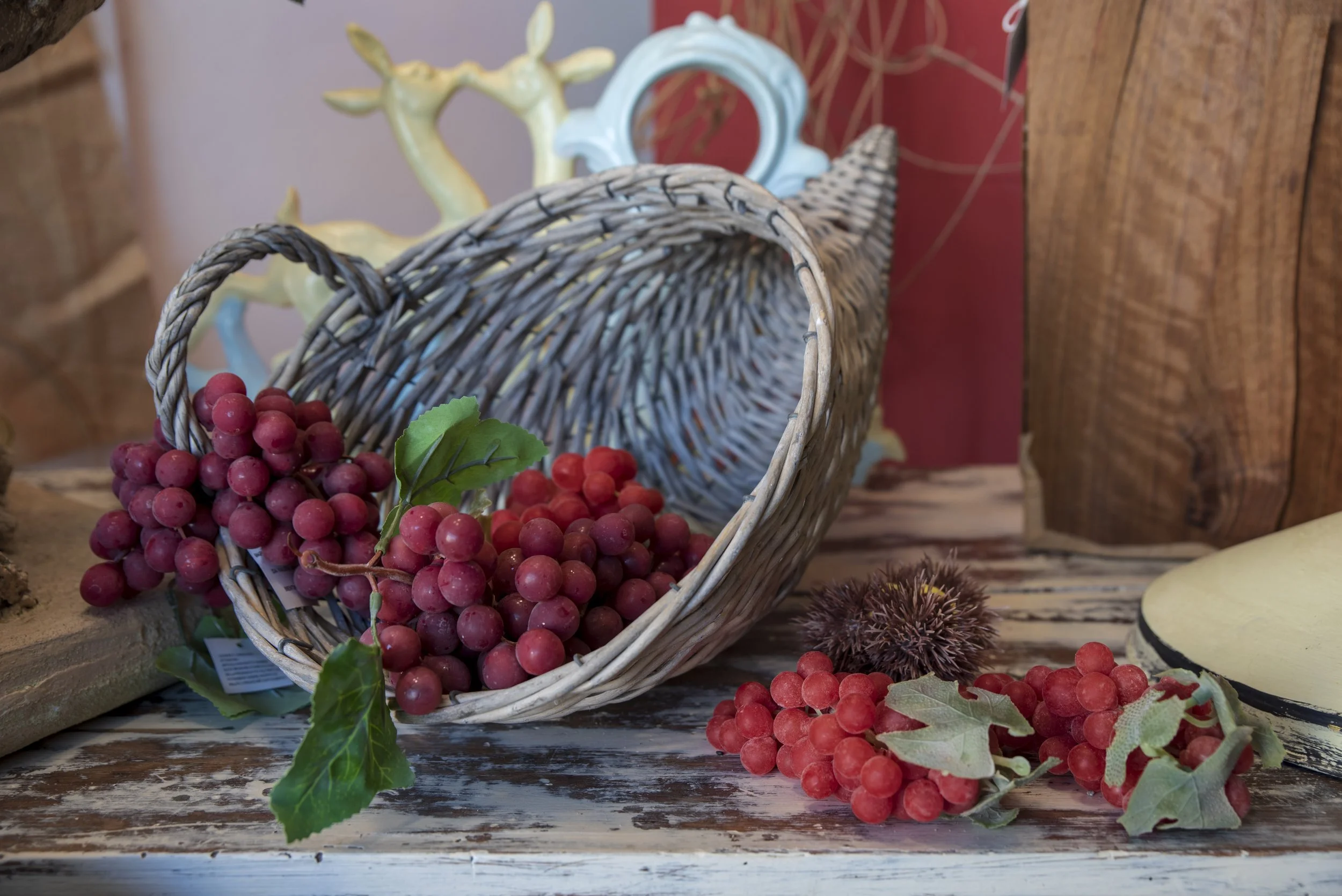 Cestino di vimini rovesciato con grappoli d'uva rossa e decorazioni su un tavolo di legno.