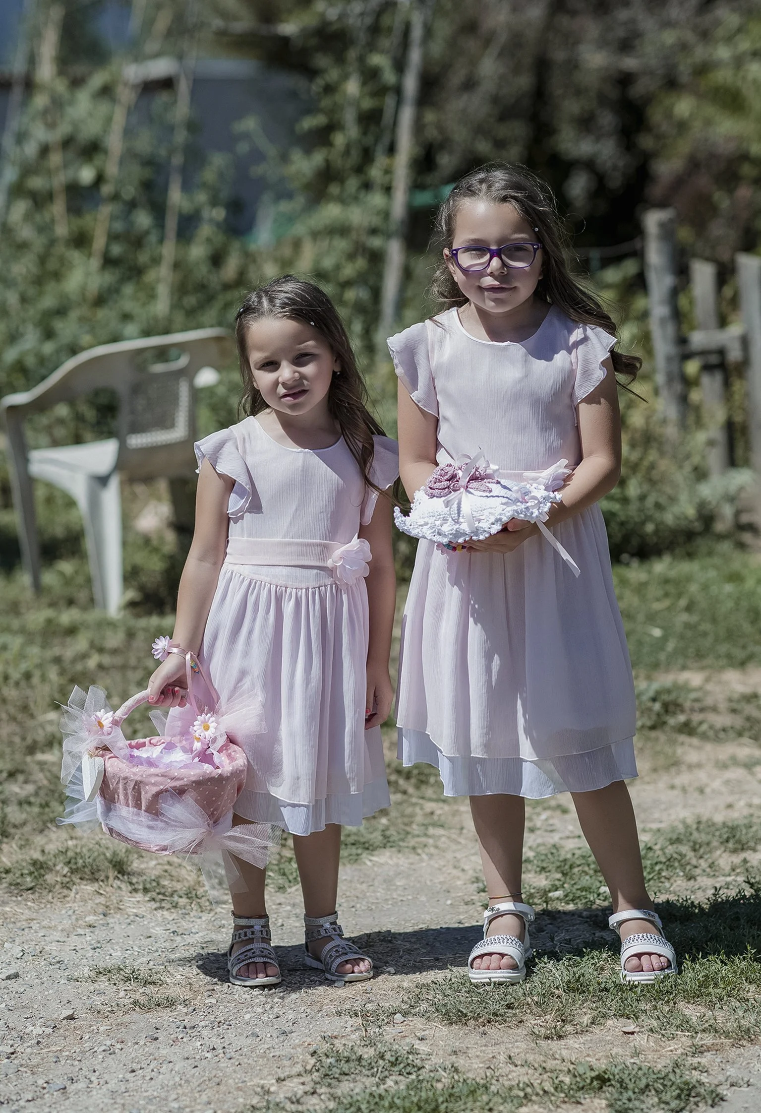 Due bambine in vestiti rosa chiaro, una con cesto di fiori, all'aperto.