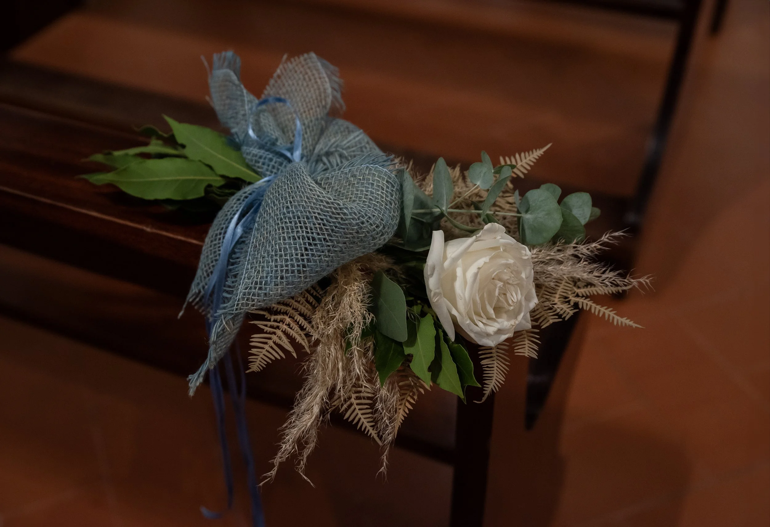 Decorazione floreale con rosa bianca, foglie verdi, rami secchi e fiocco blu.