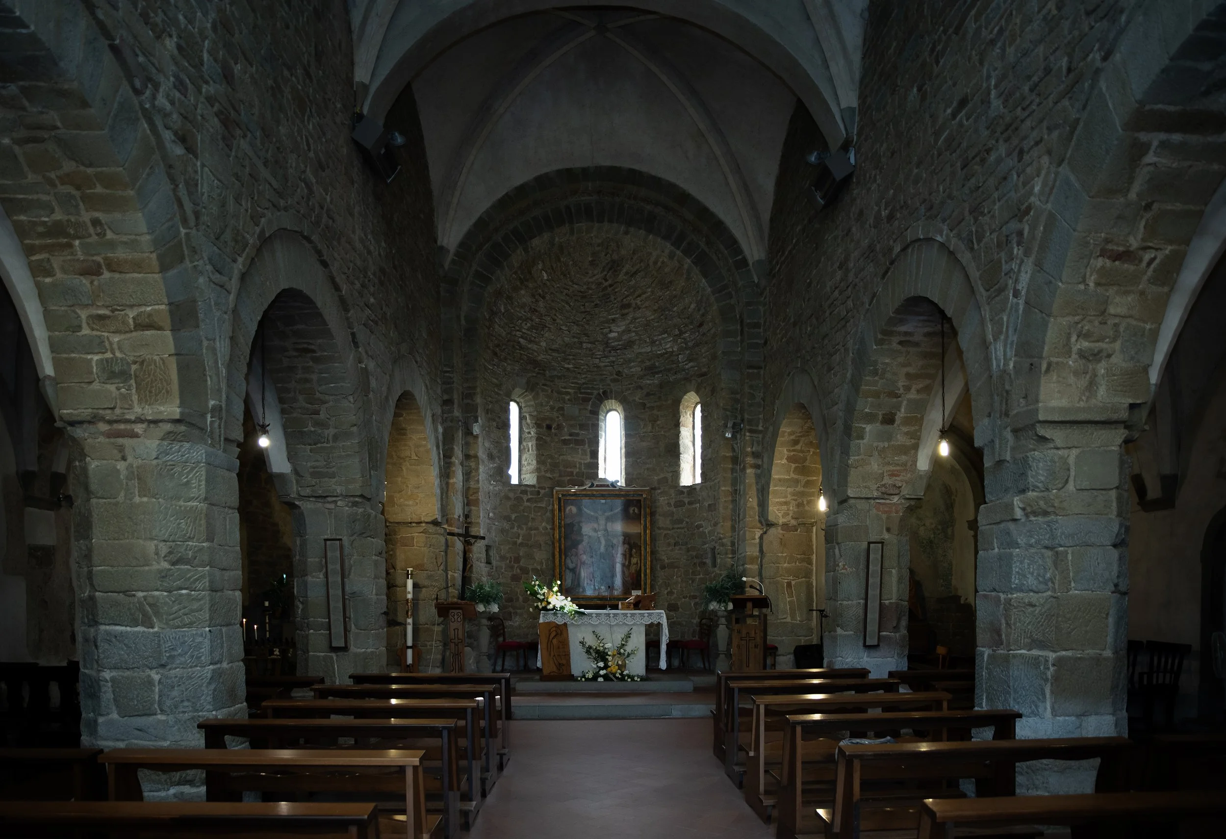 Interno di una chiesa storica in pietra con navata centrale e altare decorato.