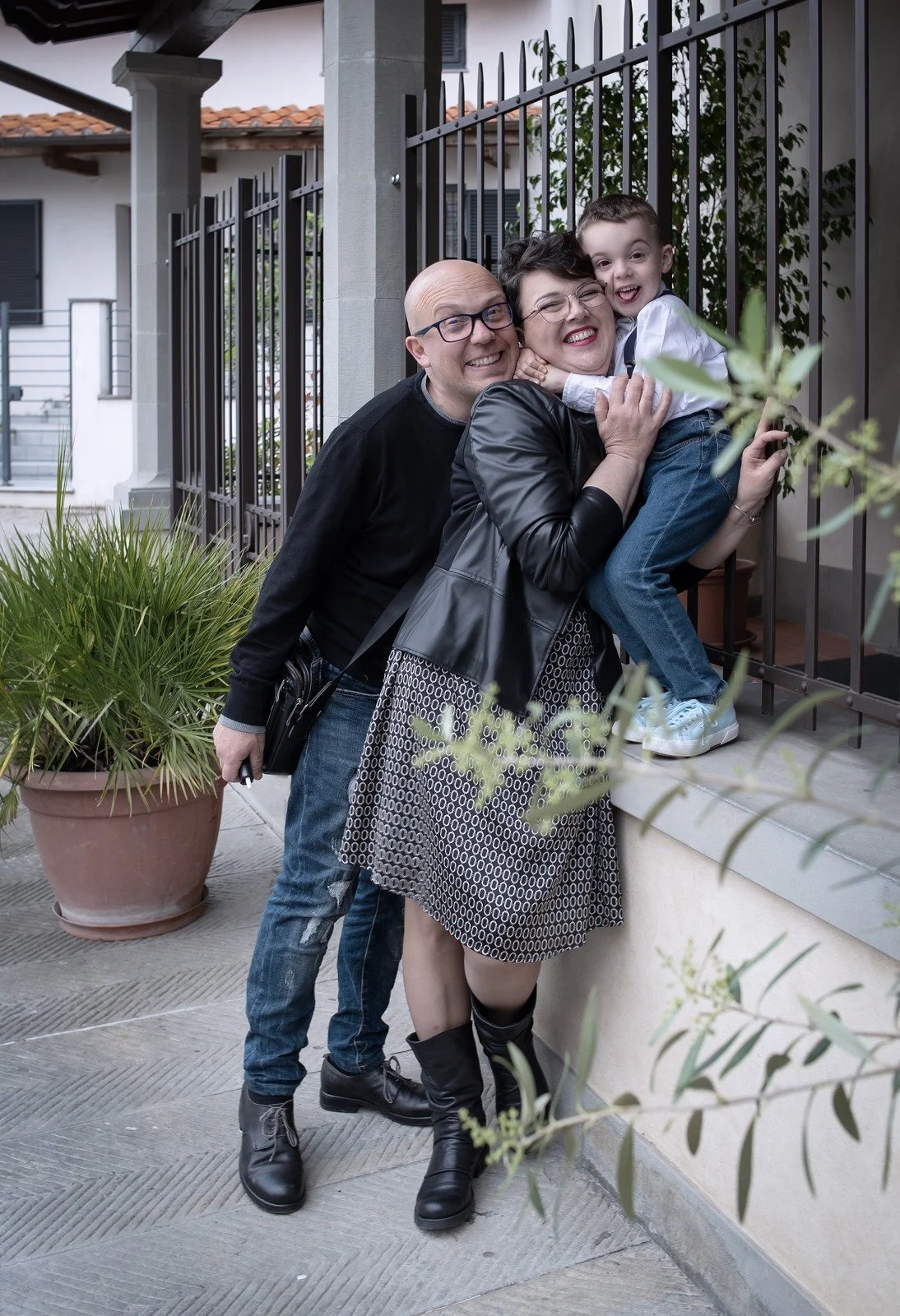 Un uomo, una donna e un bambino sorridenti posano vicino a una ringhiera all'aperto, in un ambiente urbano.