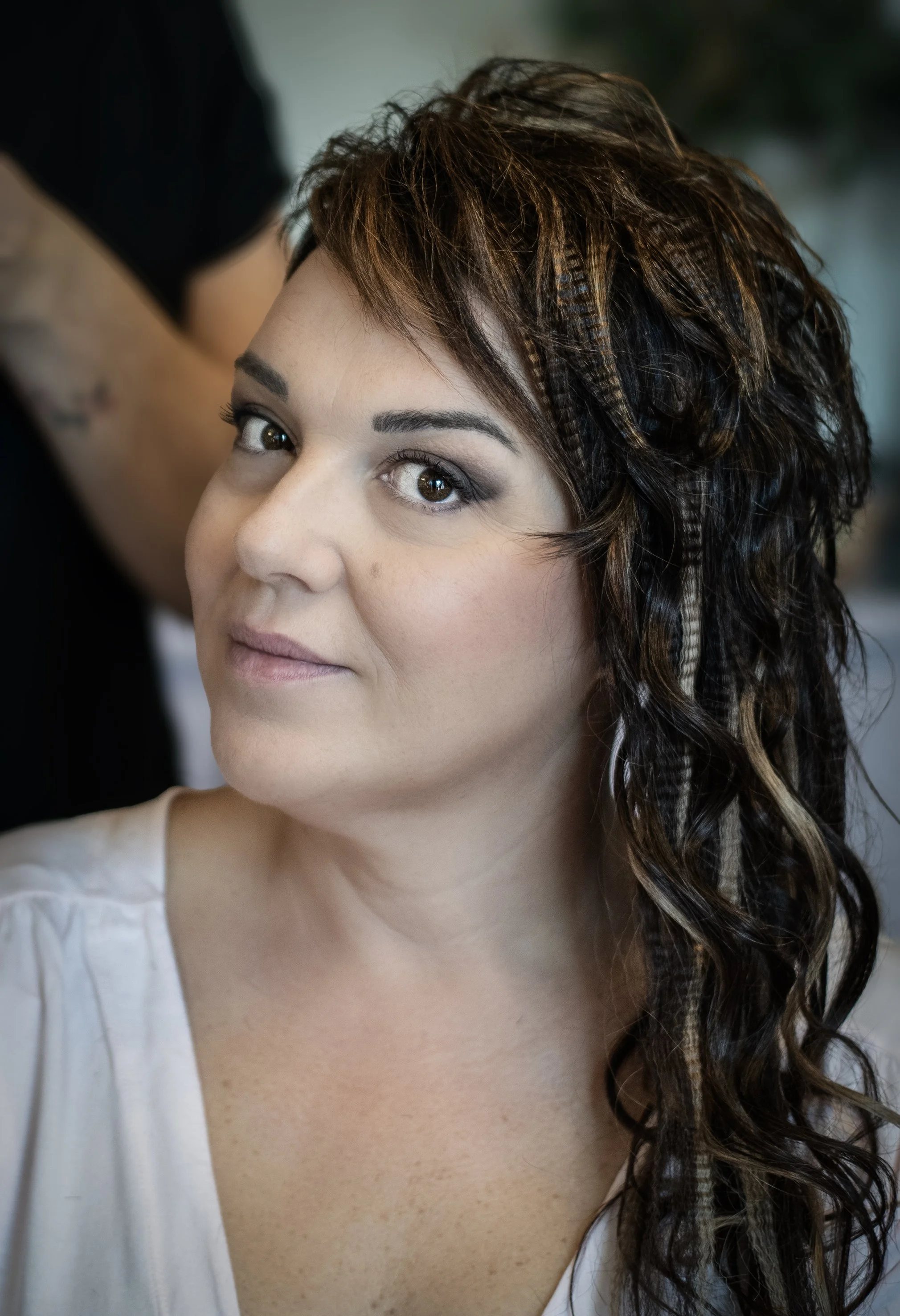 Donna con capelli ondulati e truccata, indossa una maglia bianca.