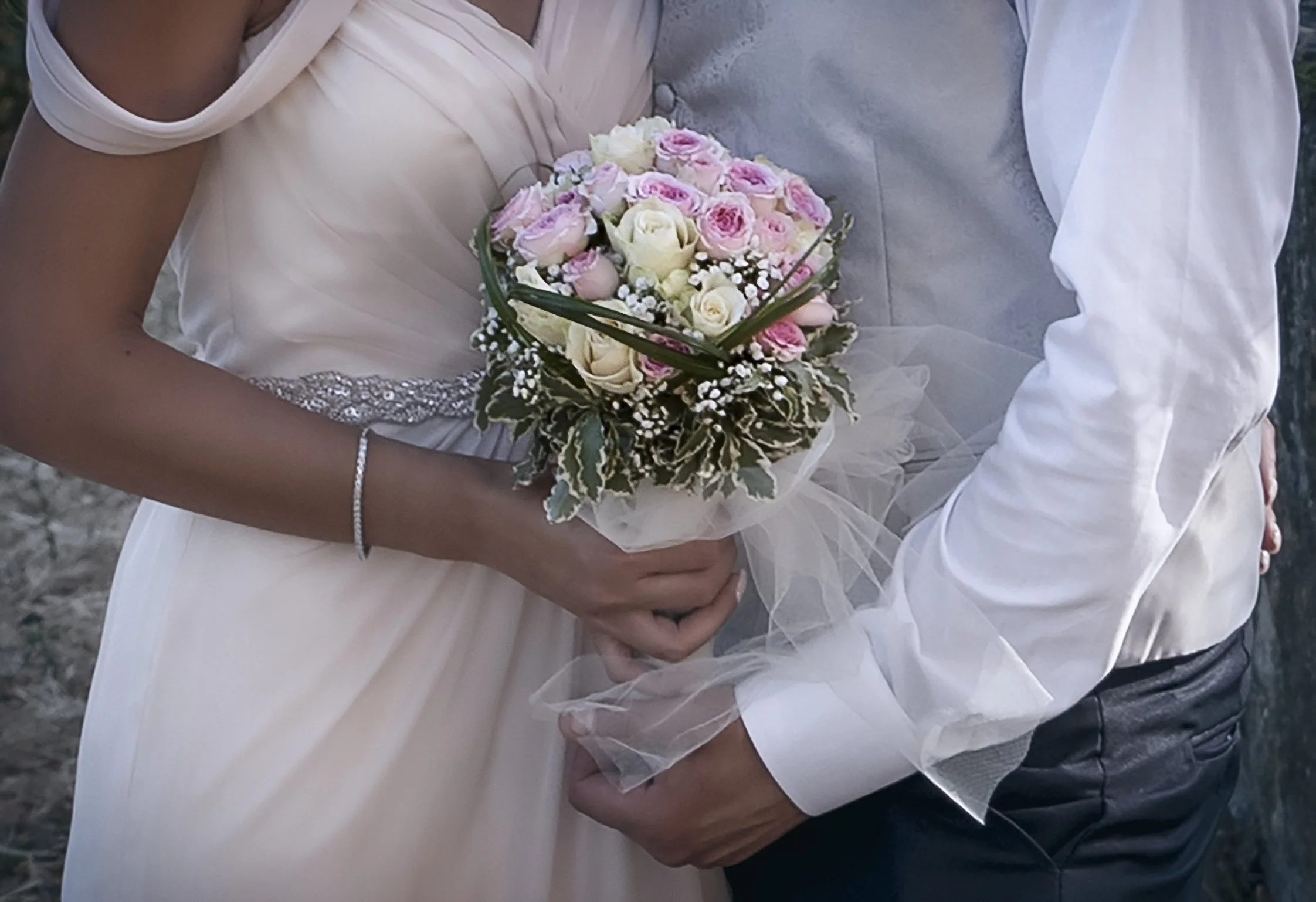 Una coppia in abiti da matrimonio che tiene un bouquet di rose bianche e rosa.