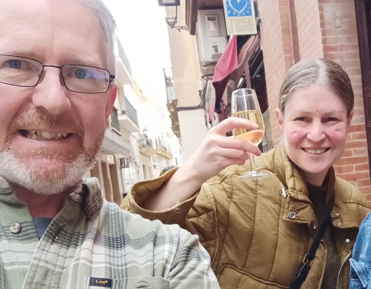 A selfie of a man and a woman. The woman is holding a glass of wine.