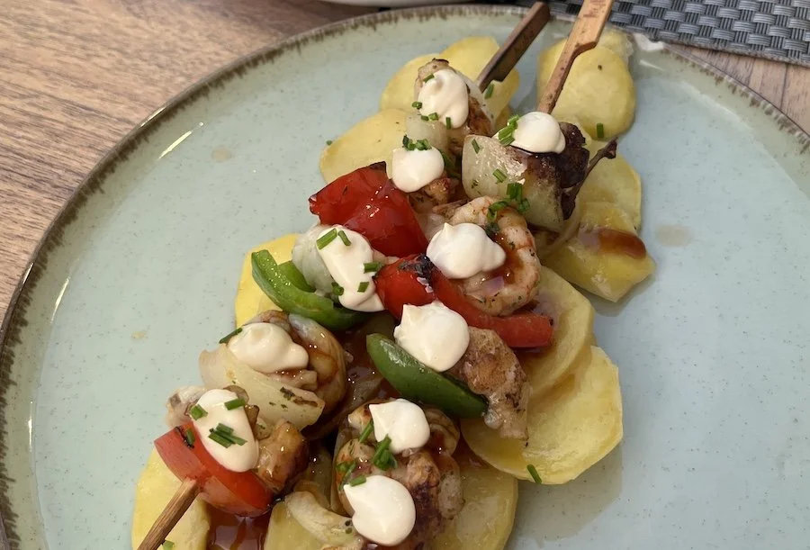 Two skewers of fish and prawns served on a bed of potatoes