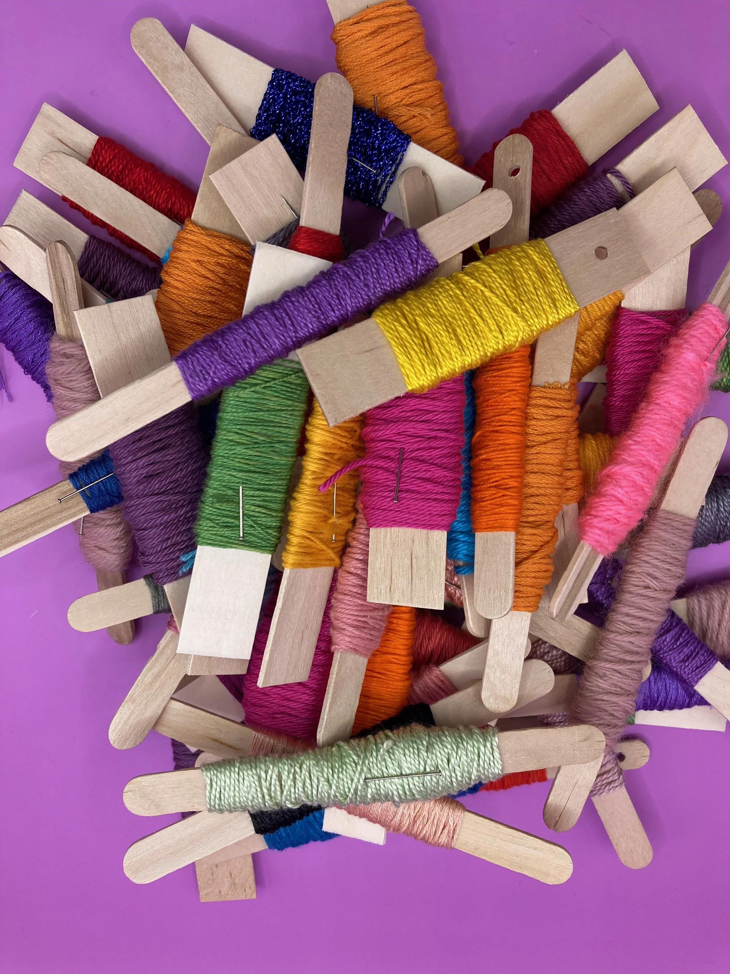 Colorful embroidery floss wound around wooden popsicle sticks on a purple background.