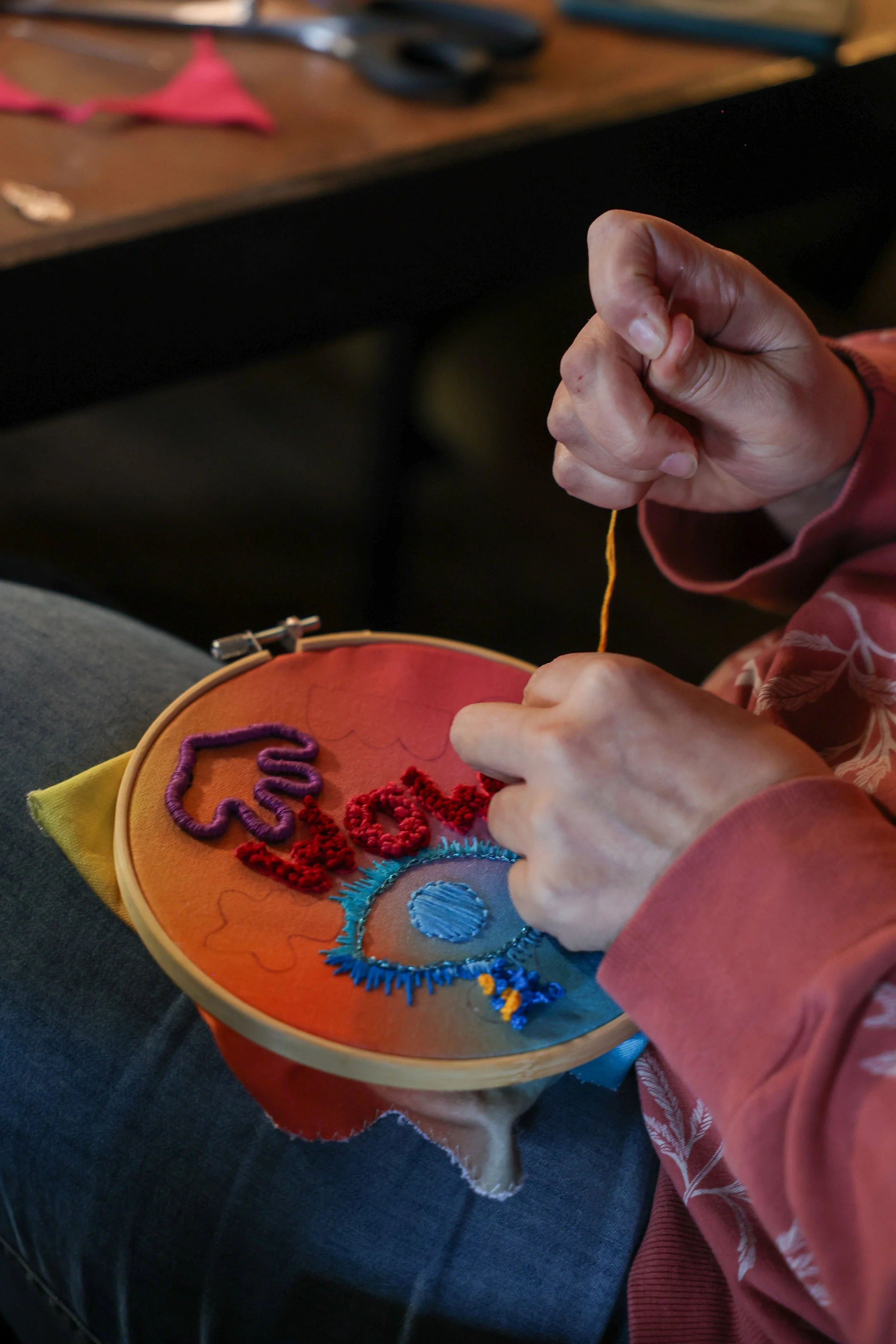Person sewing colorful embroidery with words 'Love' and 'You' on fabric in embroidery hoop.