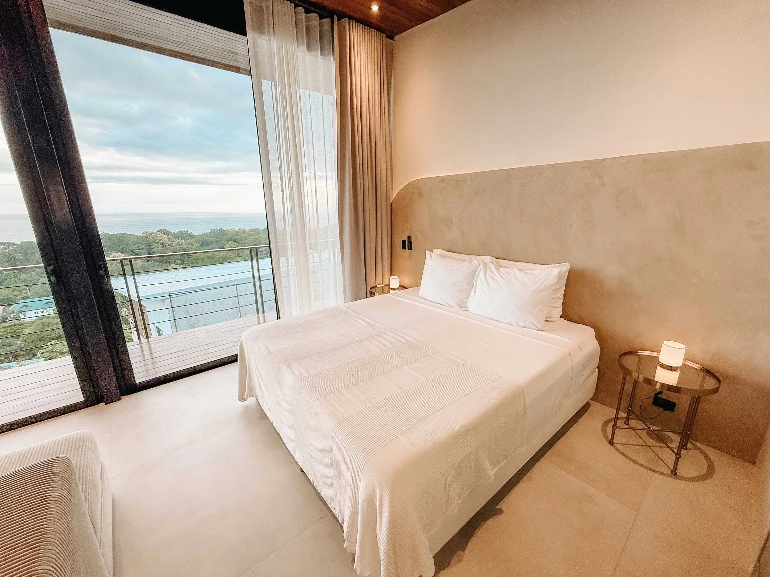 European king bed in Casa Surya beside floor-to-ceiling glass doors with views over the Pacific Ocean.