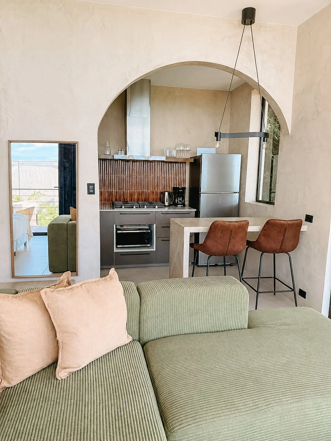 Open kitchen and dining nook framed by an arched doorway, with cozy living area seating.