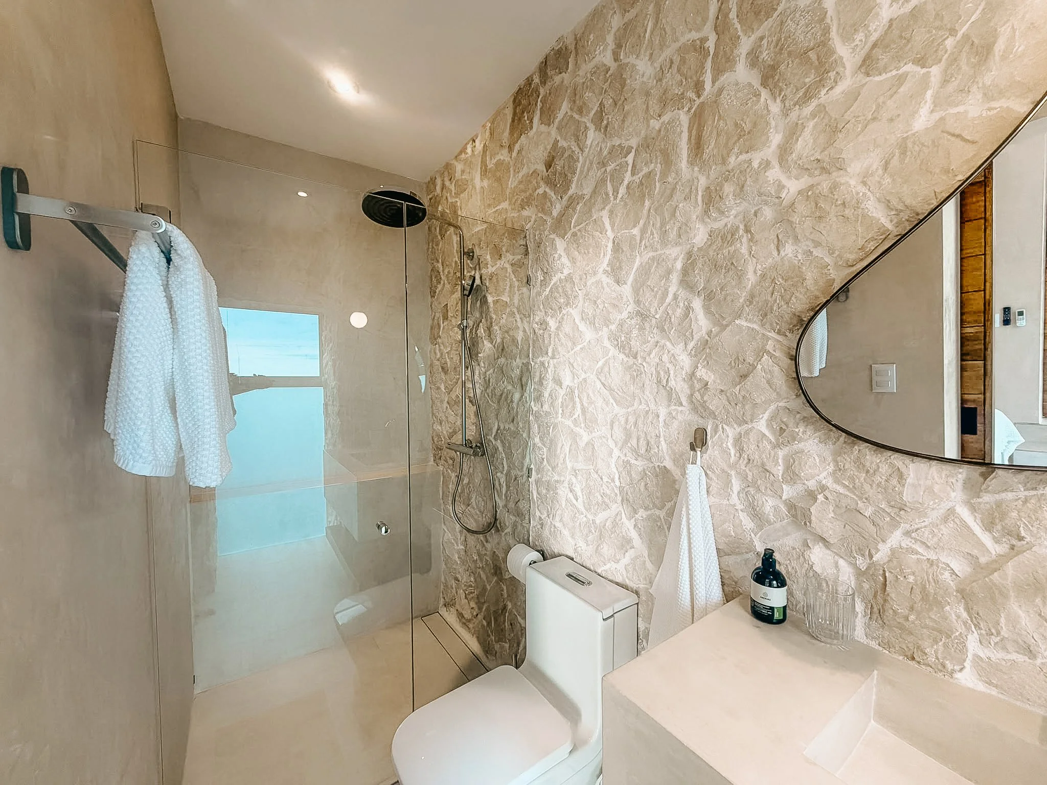 Casa Cueva bathroom with natural stone wall, walk-in rain shower and minimalist vanity.