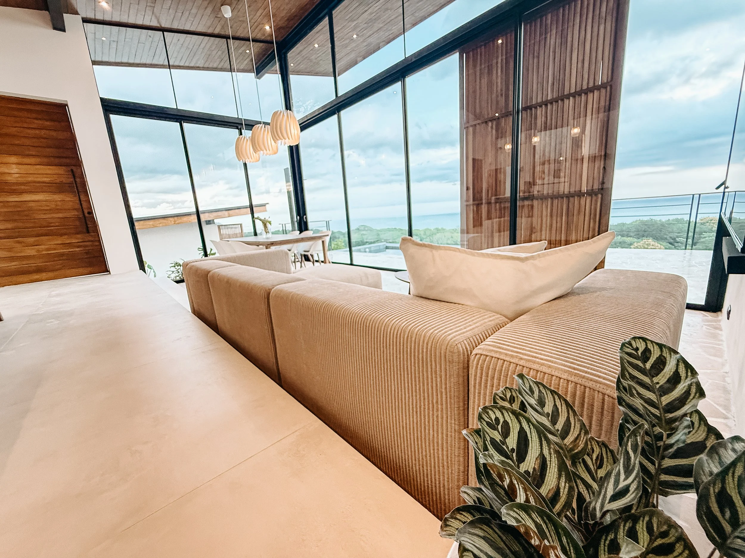 Villa Nalu living room with tropical plants, floor-to-ceiling glass walls and panoramic Pacific Ocean views.