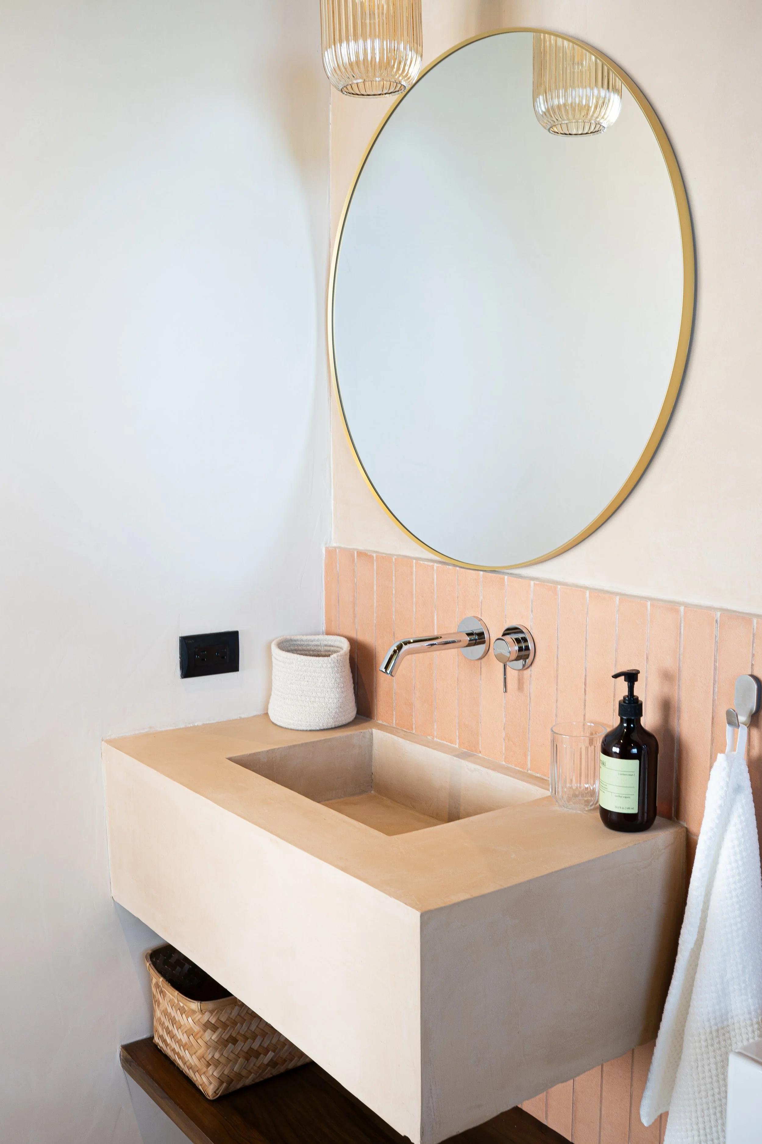 Boutique bathroom at Casa Surya with round mirror, natural plaster sink, warm tiles and soft lighting.