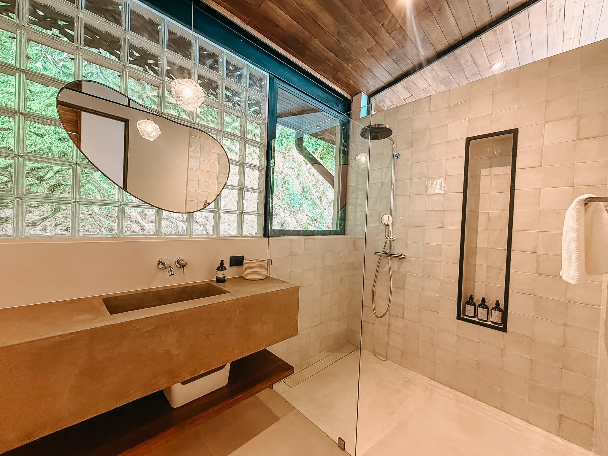 Second bathroom at Villa Nalu with a walk-in rain shower, natural finishes and a glass-block wall.