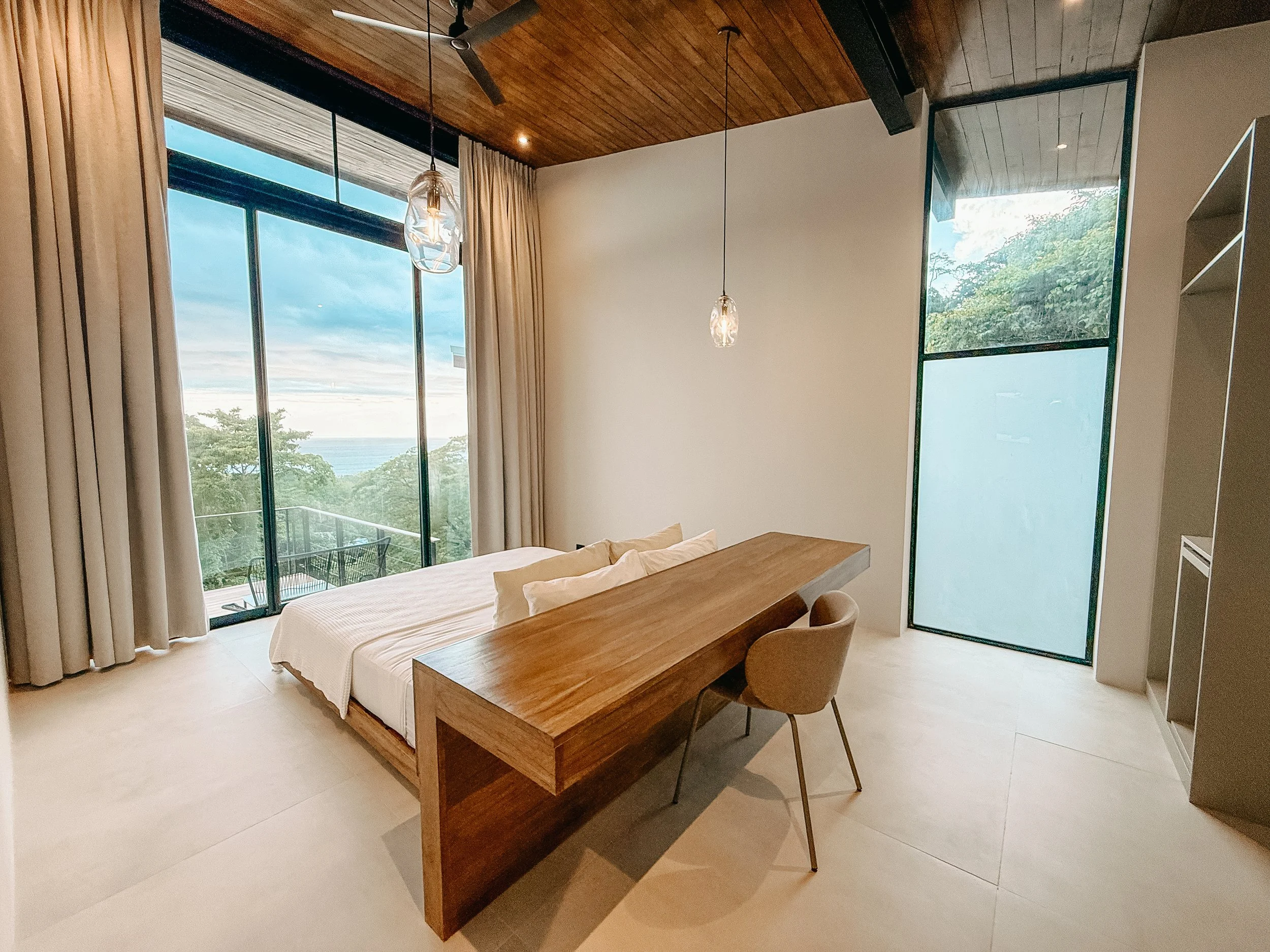 Primary bedroom at Villa Nalu with a king-size bed, ocean-view workspace and natural stone details.