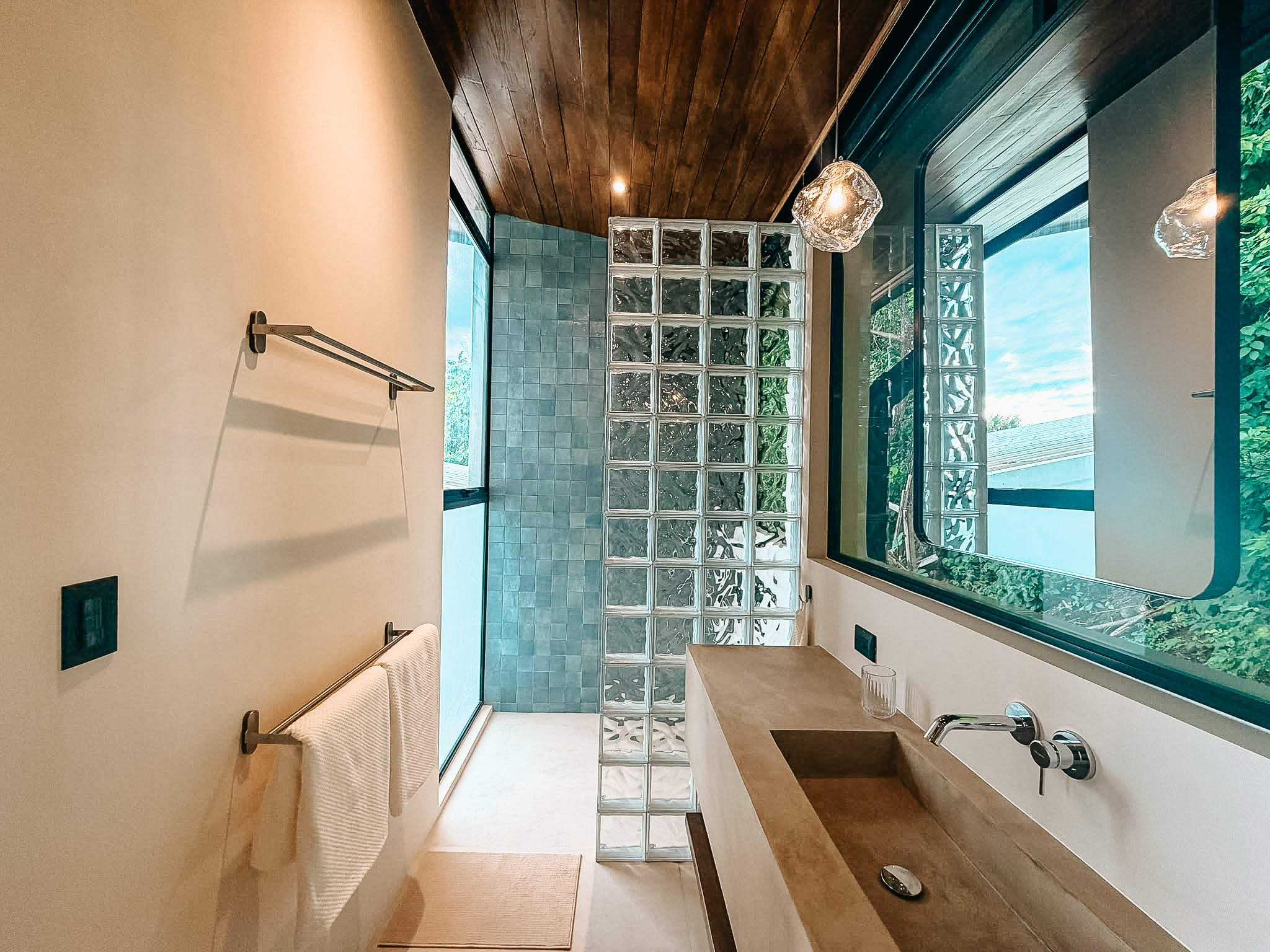 Primary bathroom at Villa Nalu with a sculpted vanity, glass-block wall and tropical natural light.