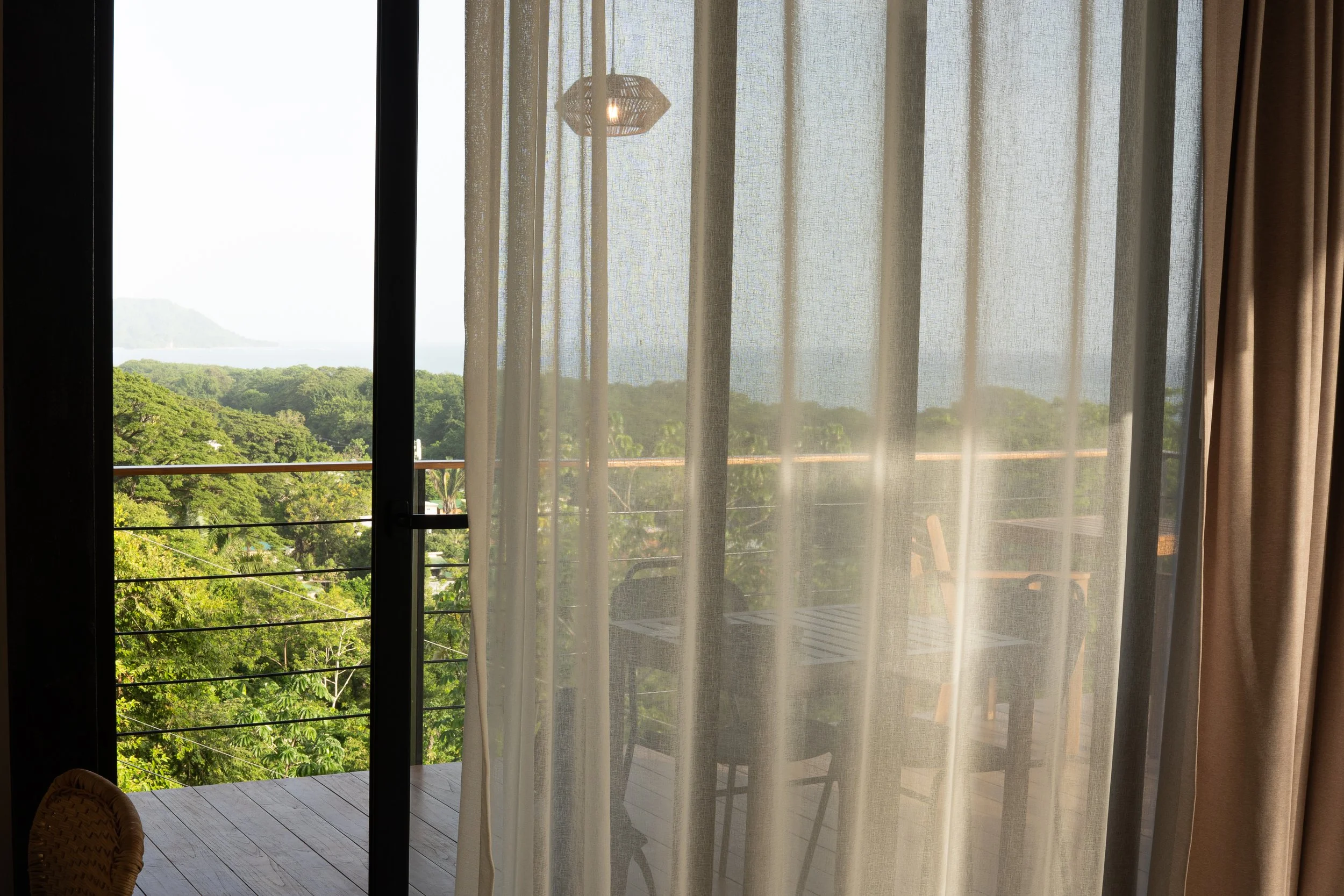 Ocean view from Casa Surya through soft curtains, overlooking the jungle and coastline of Santa Teresa.