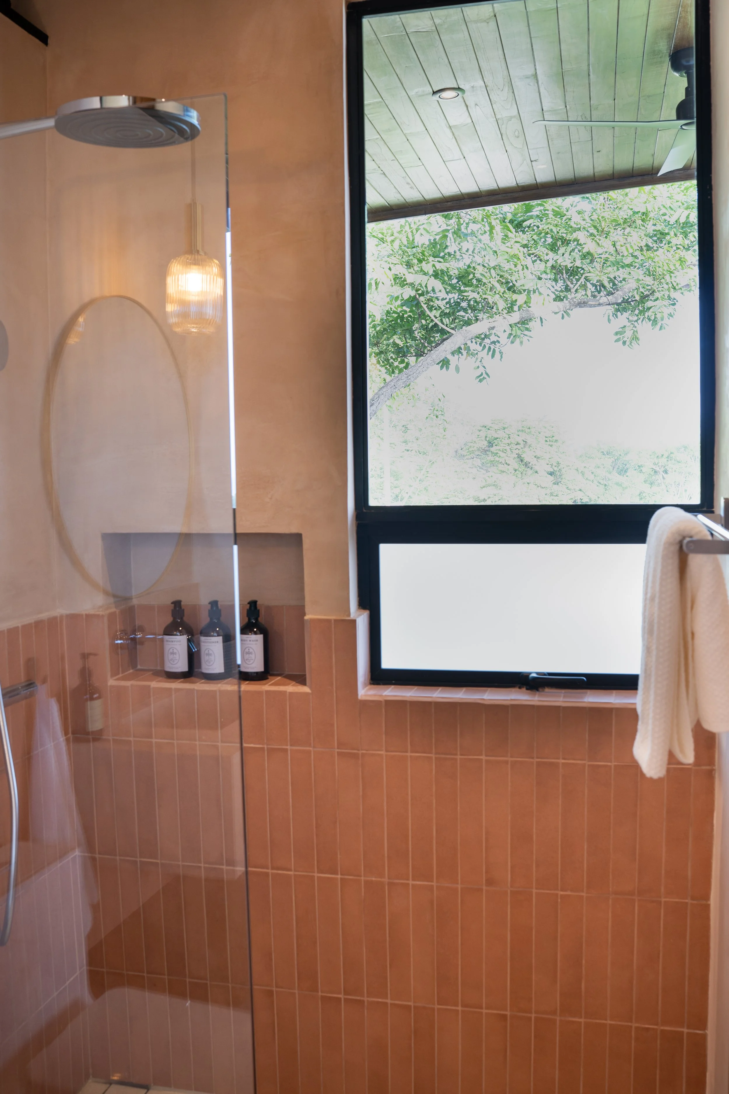 Casa Surya bathroom with walk-in shower, warm tiles, boutique amenities and tropical view through the window.