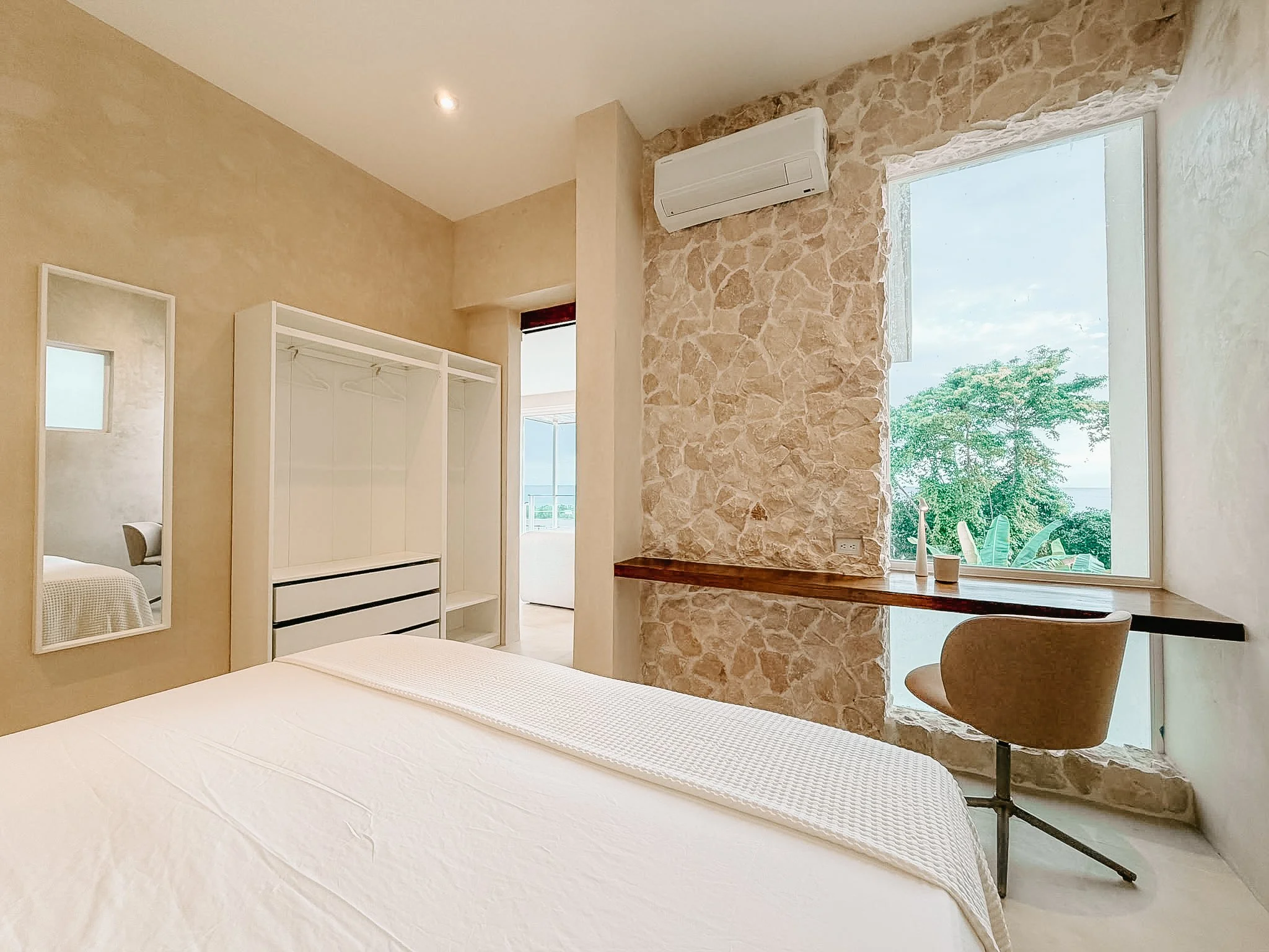 Primary bedroom at Casa Cueva with a European king bed, built-in workspace, natural stone wall and ocean view.
