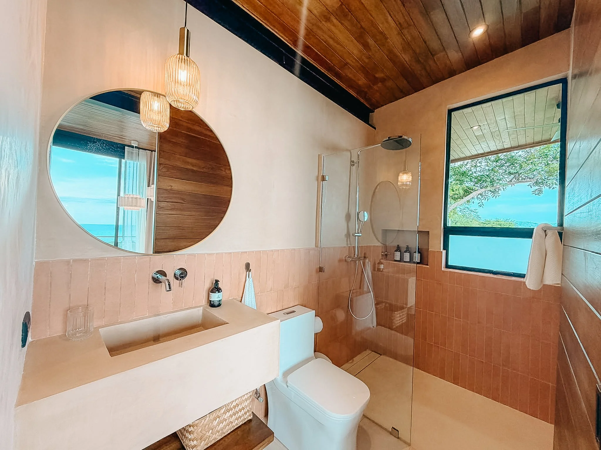 Casa Surya bathroom with warm terracotta tiles, a round mirror and a walk-in rain shower.