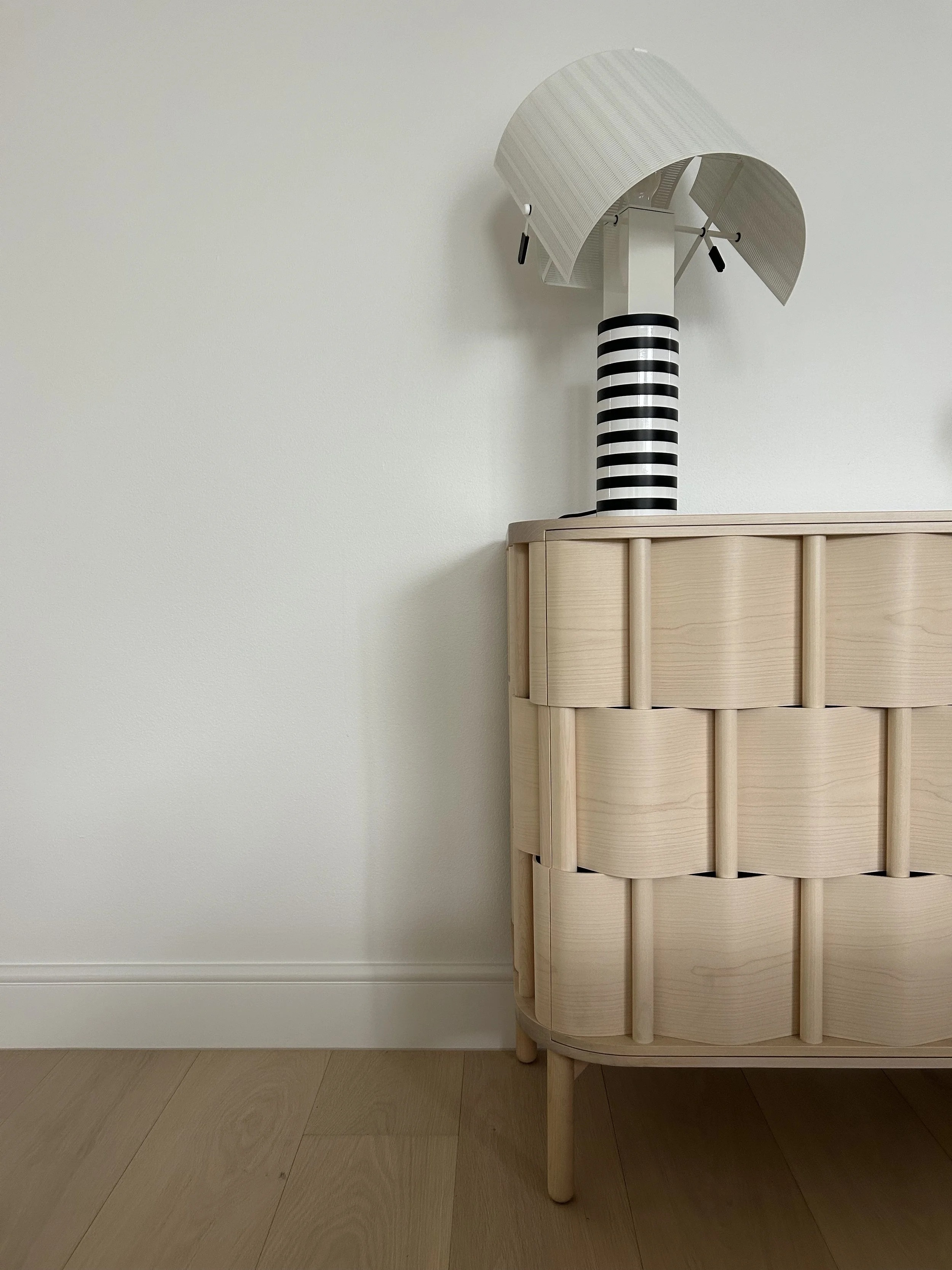 A bedside table made of light-colored wood with a decorative design, on which rests a modern lamp with a striped black and white cylindrical base and a curved lampshade.