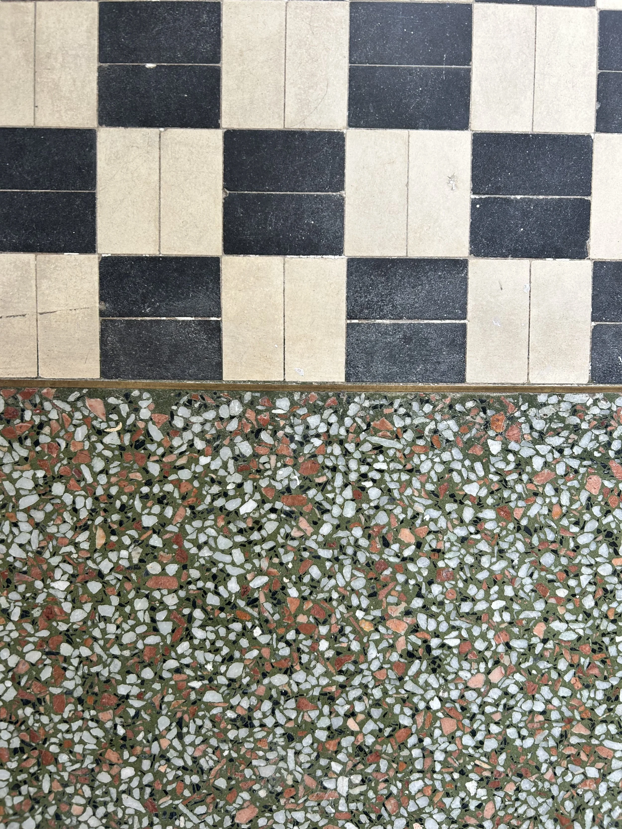 Close-up of two different types of flooring: a black and beige checkered tile pattern at the top and a multicolored terrazzo surface at the bottom.