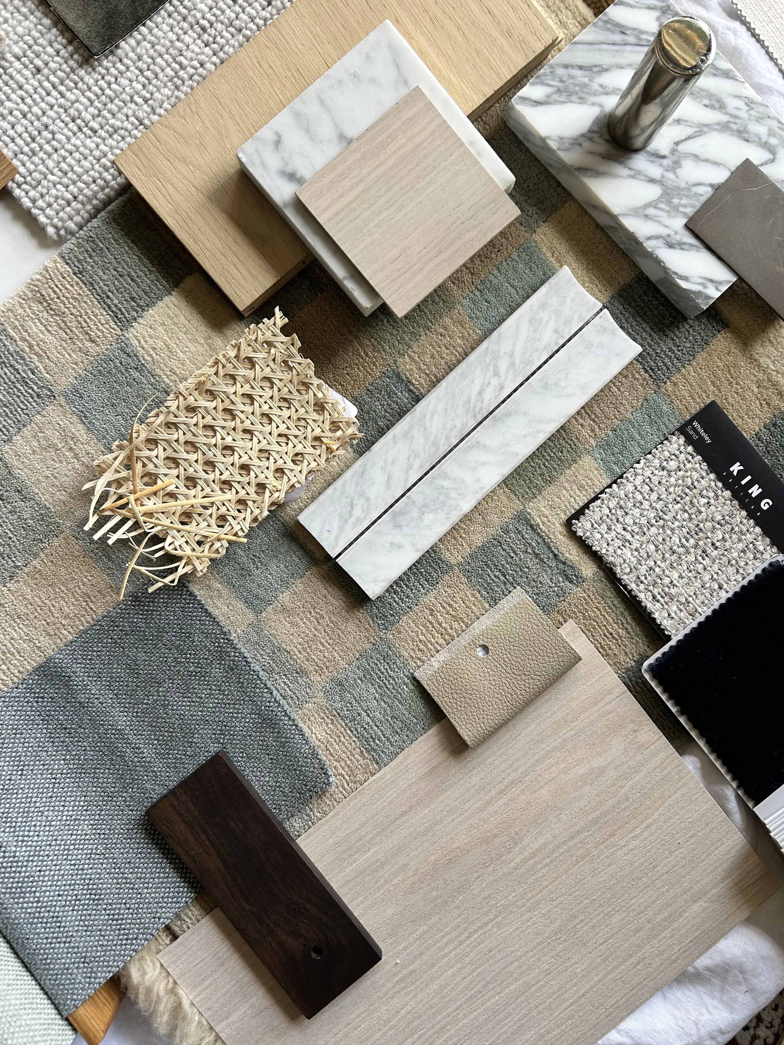 An assortment of tile and fabric samples, including wood, marble, and textile textures, spread out on a checkered rug.