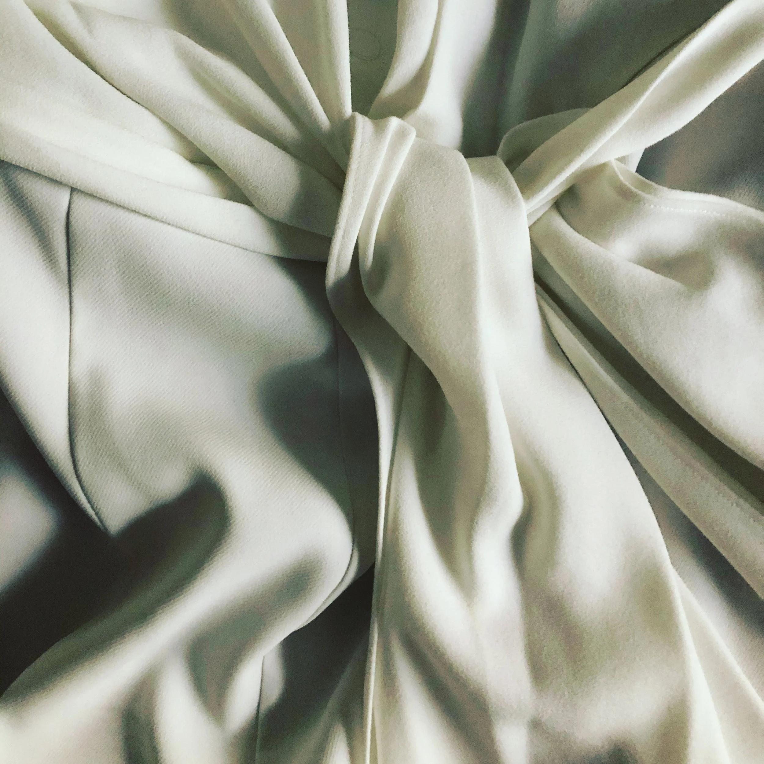 Close-up of a fabric with a knotted tie detail, showing light-colored satin and matte material with smooth texture.